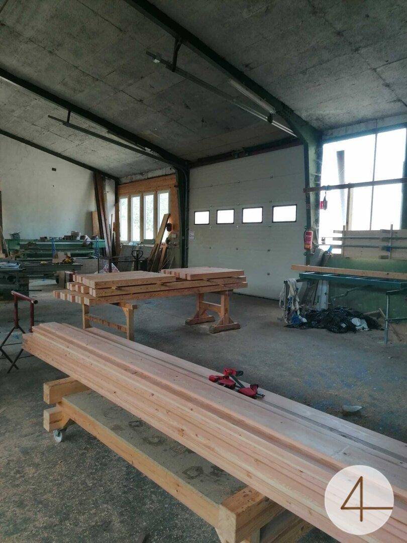 Werkstattraum mit Betonboden, Holzstapeln und einem großen Rolltor im Hintergrund.