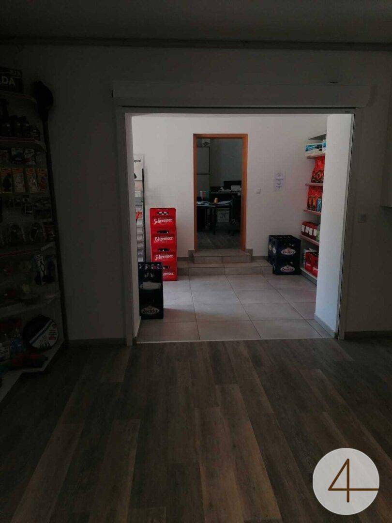Innenraum eines Ladenlokals mit Holzboden und einem Durchgang zu einem weiteren Raum.