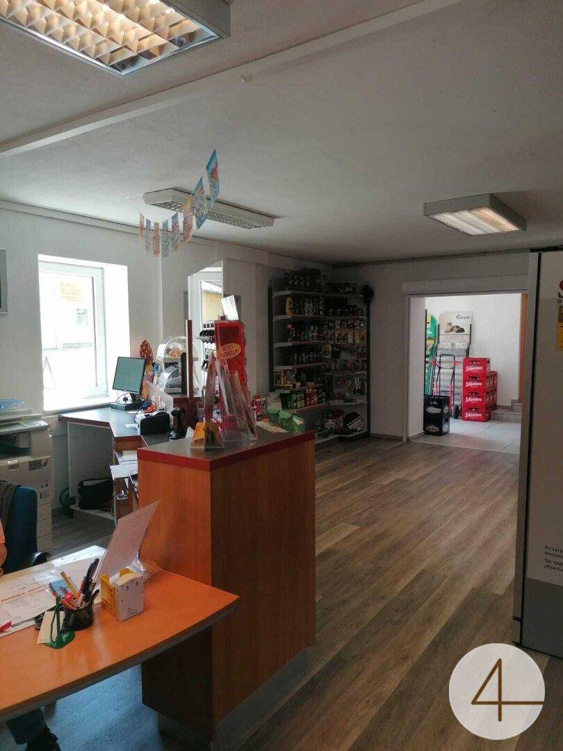 Heller Verkaufsraum mit Theke, Regalen und einem Arbeitsplatz am Fenster, ausgestattet mit modernen Deckenleuchten.