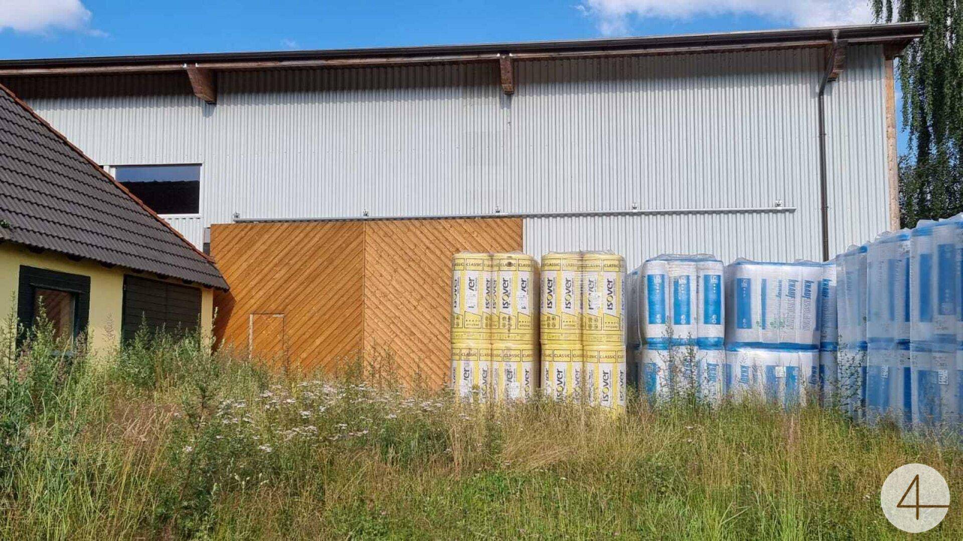 Fassade eines Industriegebäudes mit Holzverkleidung und gestapelten Baumaterialien im Vordergrund.