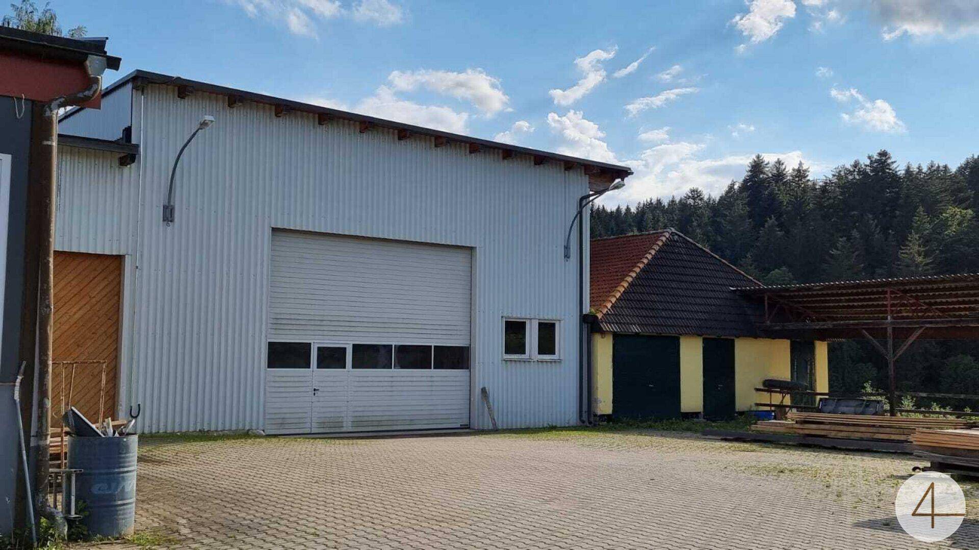 Industriegebäude mit großem Rolltor und kleineren Fenstern, daneben ein älteres Gebäude.