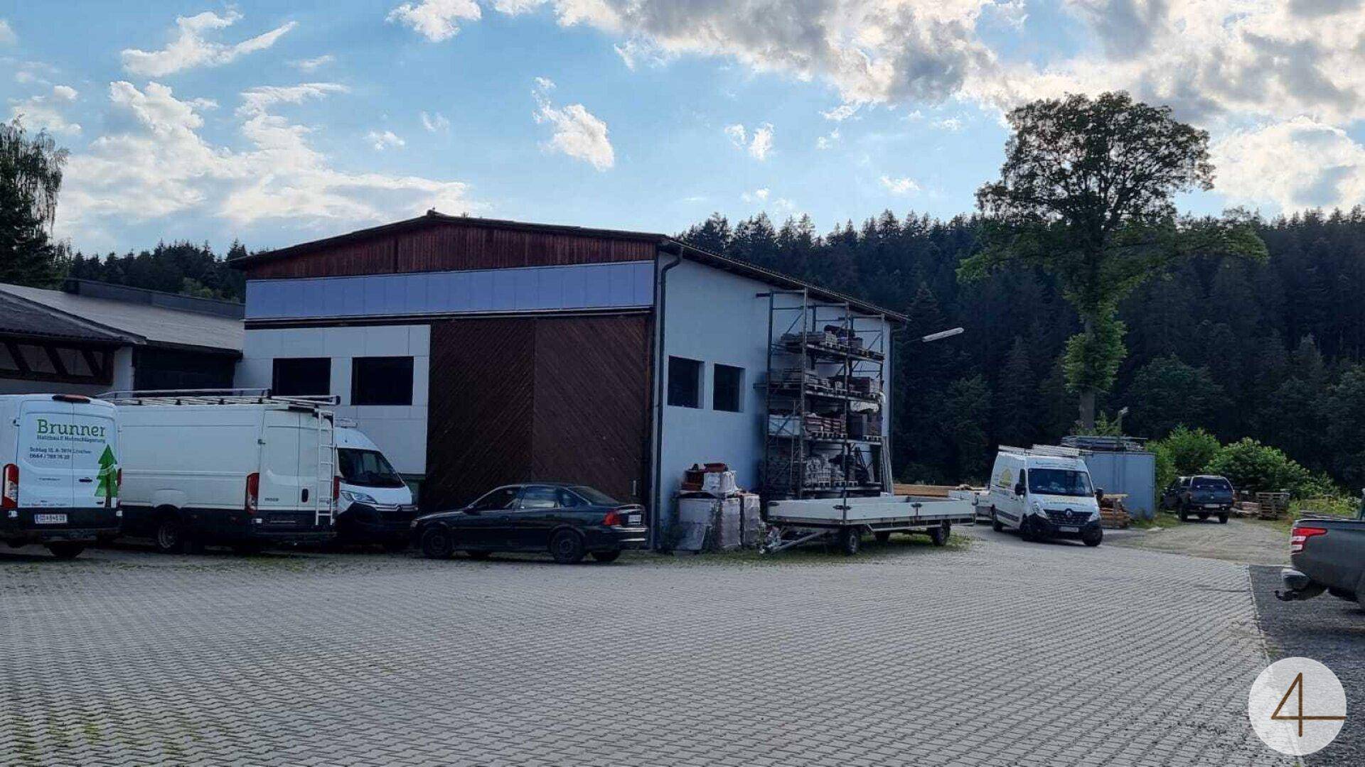 Mehrere Lieferwagen und ein Auto parken auf einem großen gepflasterten Hof vor Betriebsgebäuden.