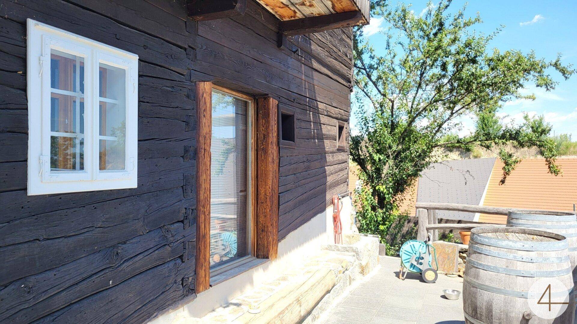 Rustikale Holzfassade eines Gebäudes mit kleinen Fenstern und einem gepflasterten Außenbereich.