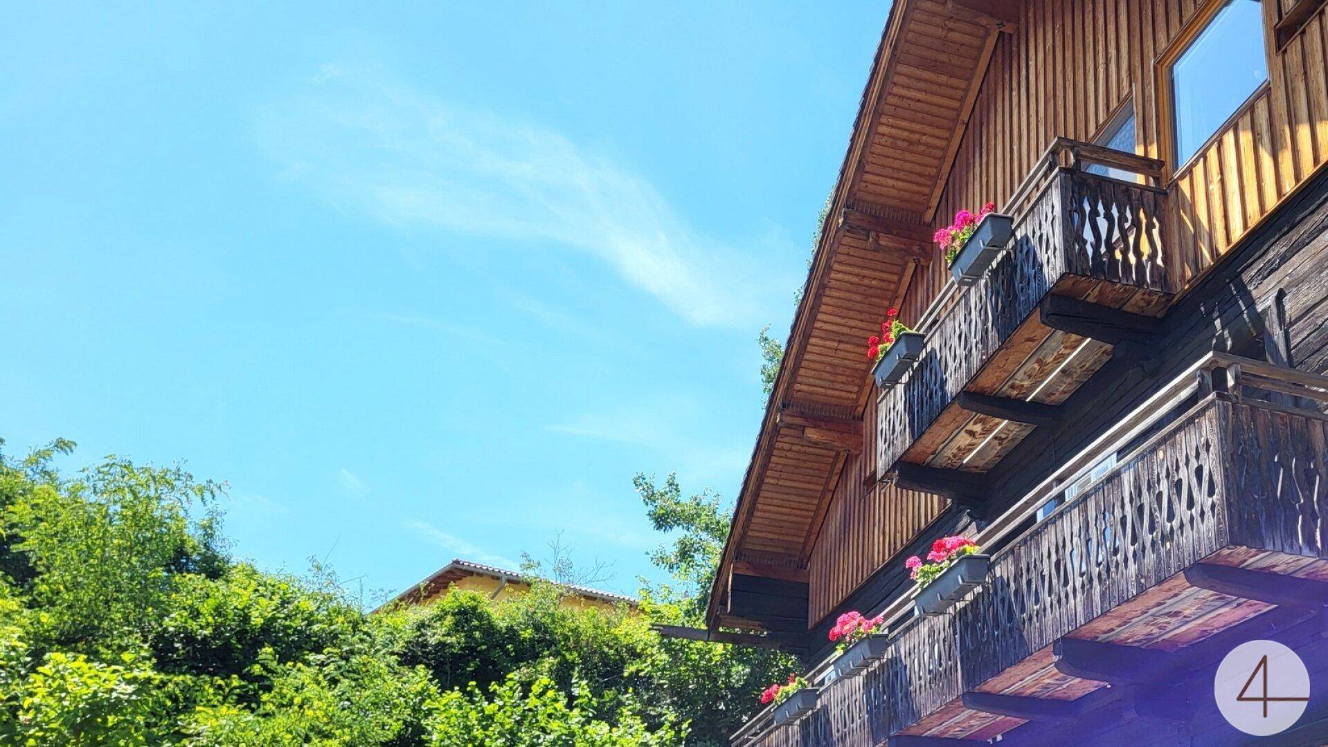 Traditionelles Holzhaus mit mehreren Balkonen und Blumenkästen unter blauem Himmel.