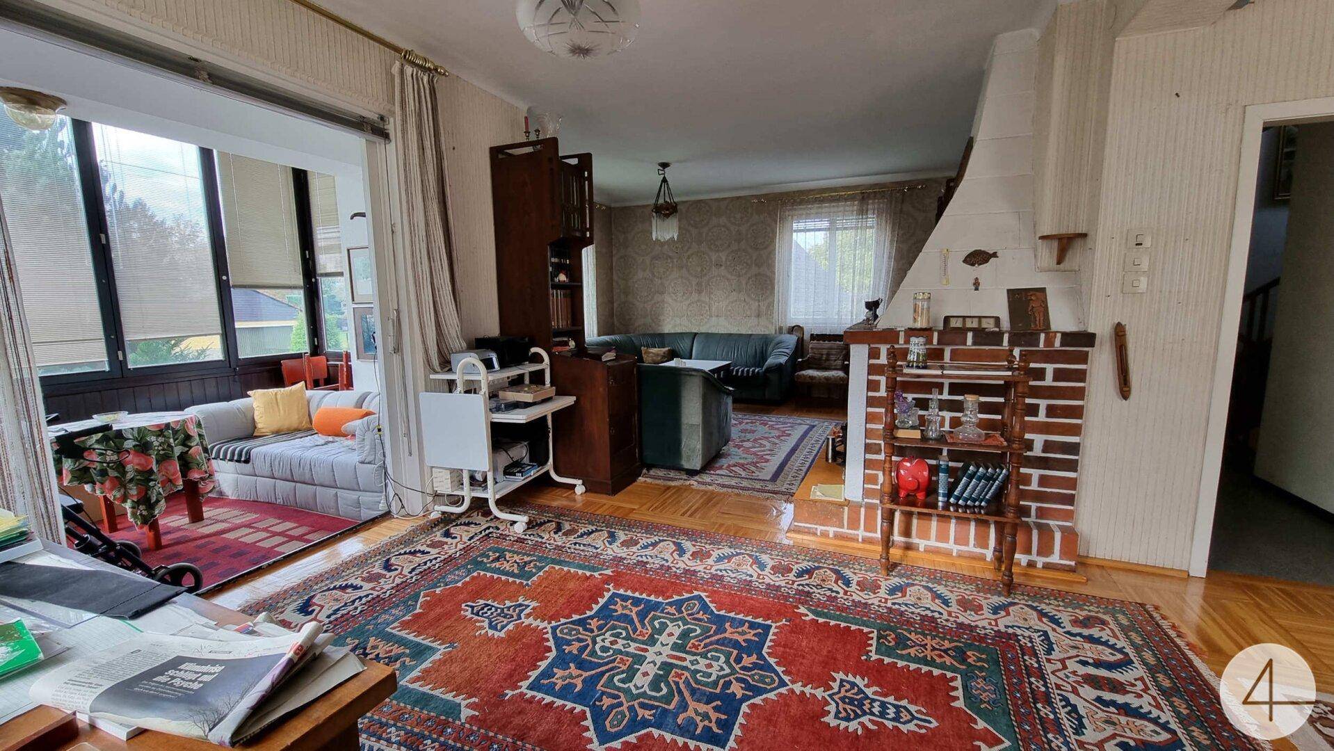 Geräumiges Wohnzimmer mit Kamin, Holzboden und Zugang zu einem hellen Wintergarten.