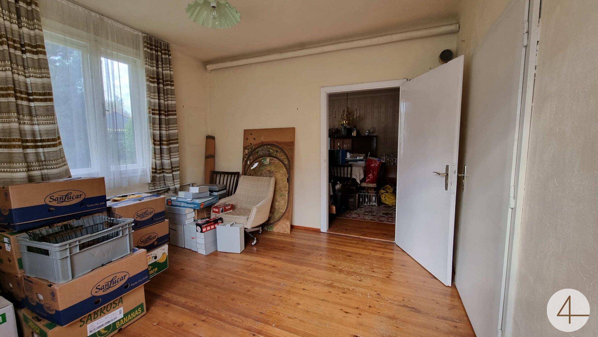 Zimmer mit Holzboden und Fenster, derzeit als Abstellraum genutzt, mit viel Tageslicht.