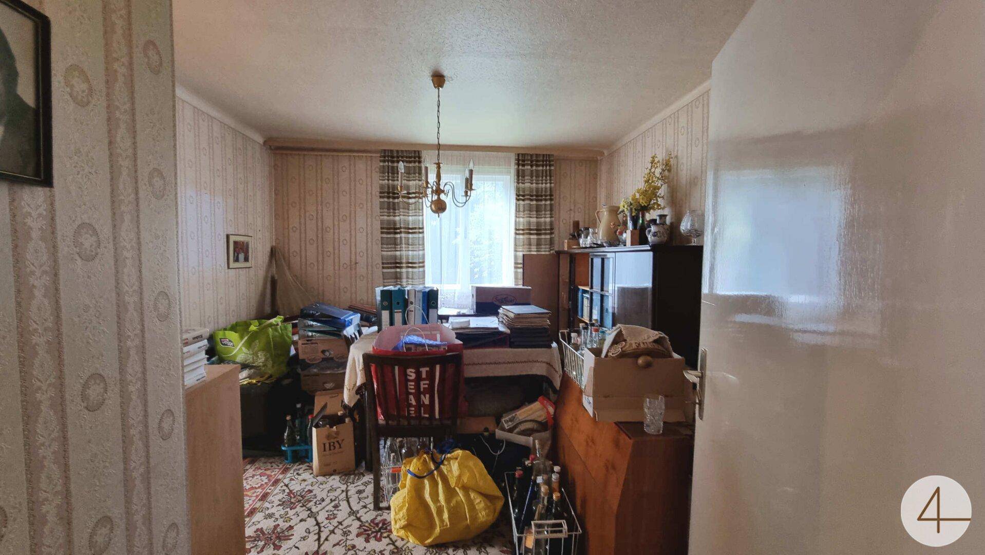 Esszimmer mit gemusterter Tapete, Kronleuchter und einem großen Tisch, hell und einladend.