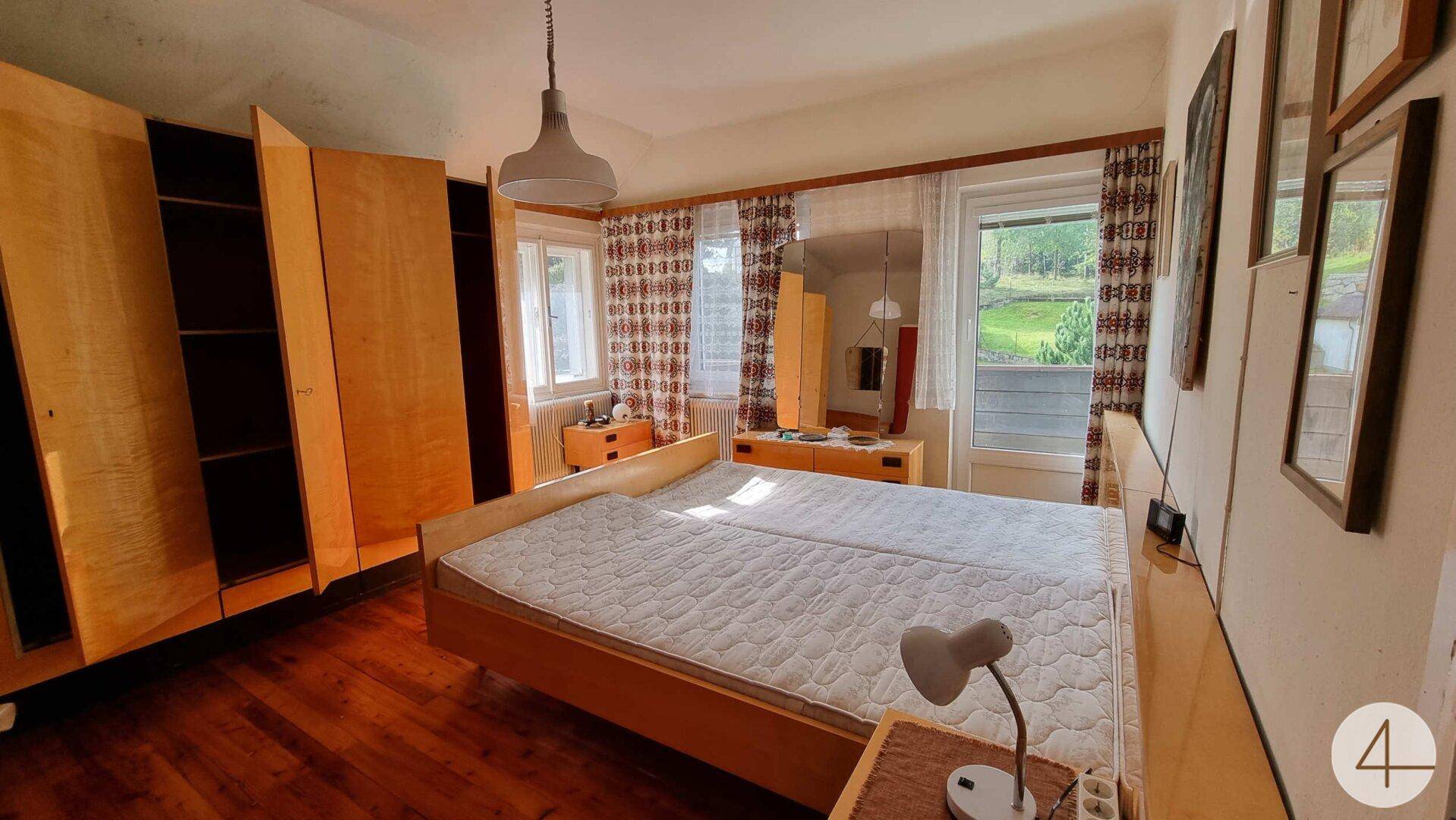 Schlafzimmer mit Doppelbett, Holzschränken und Fenstern mit Blick ins Grüne.