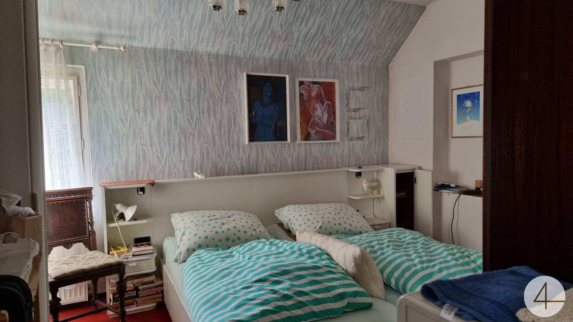 Schlafzimmer mit Doppelbett, gemusterter Tapete und Kunstwerken an der Wand.