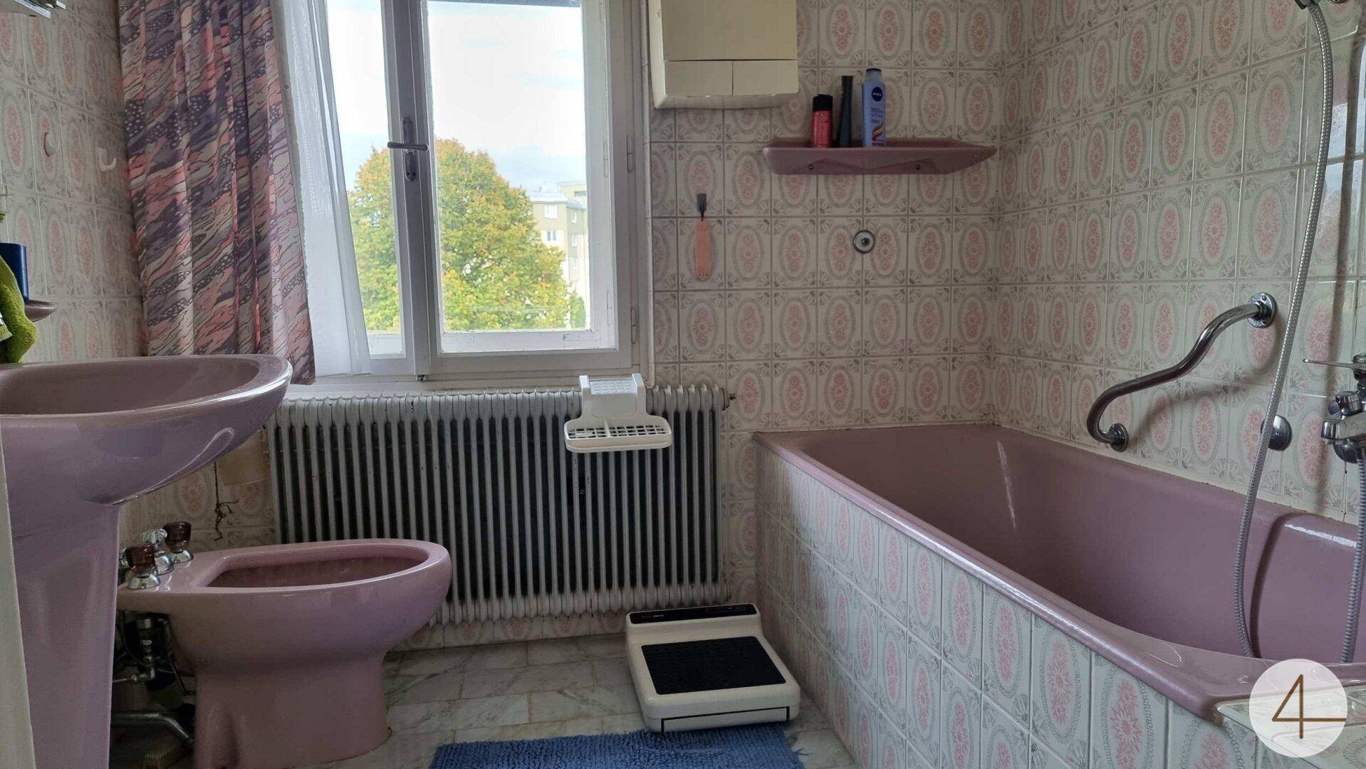 Badezimmer im Stil der 80er Jahre mit rosa Sanitärobjekten, gemusterten Fliesen und Fenster.