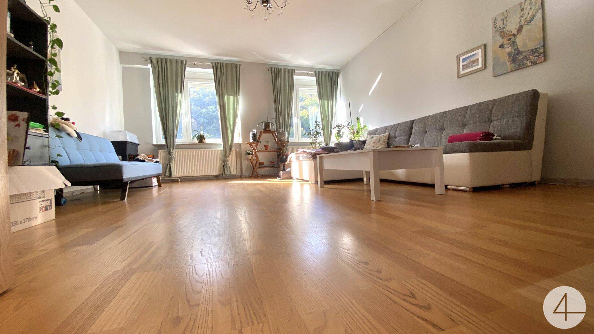 Helles Wohnzimmer mit Holzfußboden, bequemen Sofas und großen Fenstern, die viel Tageslicht hereinlassen.