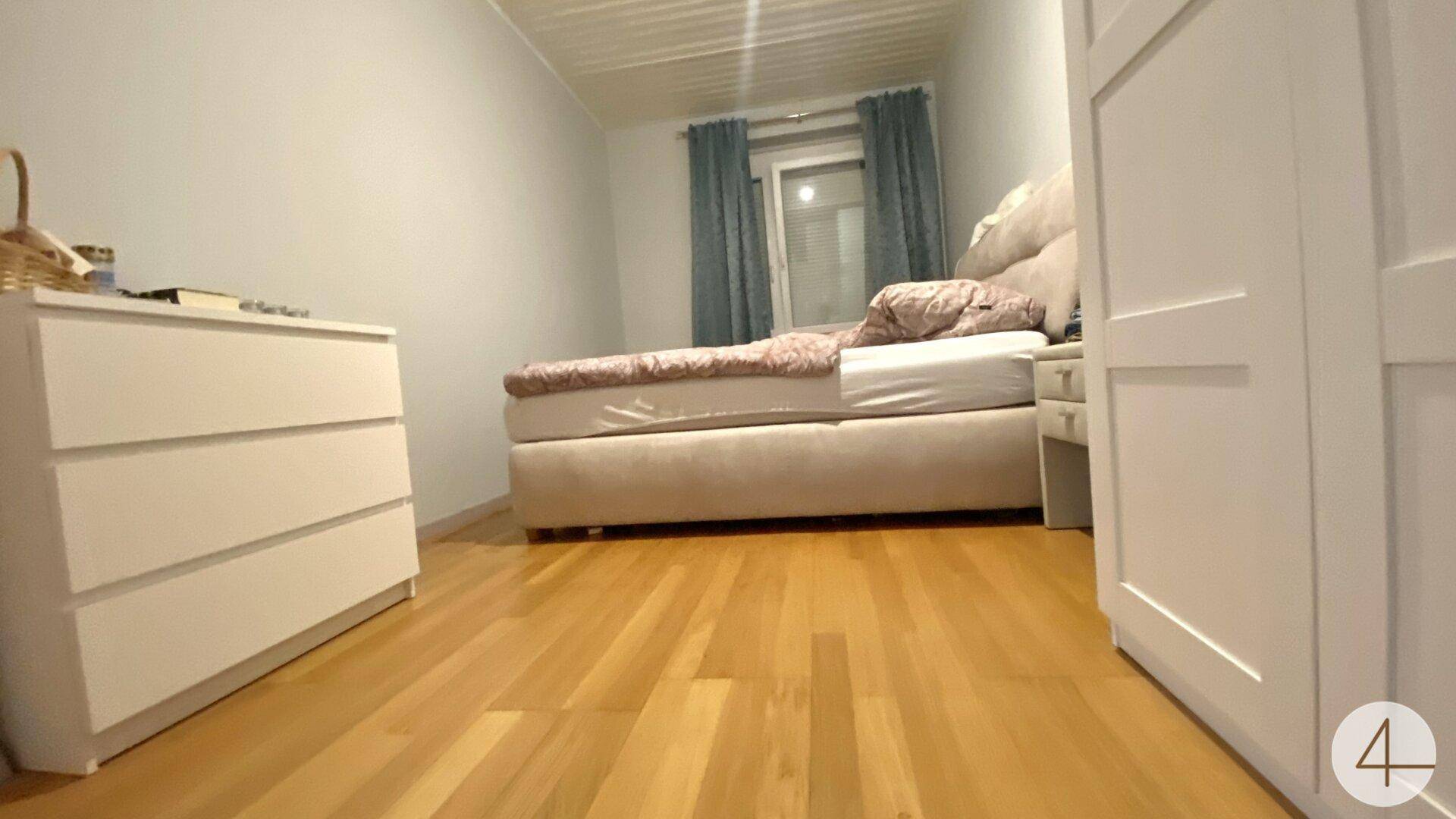 Gemütliches Schlafzimmer mit hellem Holzfußboden, einem bequemen Bett und einem weißen Kleiderschrank.