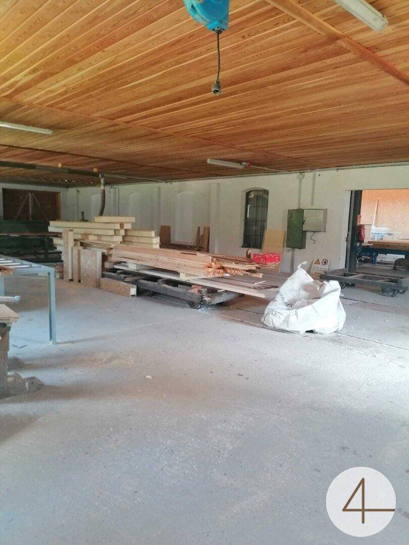 Großer Werkstattraum mit Holzdecke, Betonboden und gestapelten Holzmaterialien.