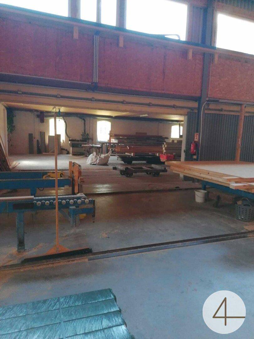 Große Werkshalle mit Betonboden, Holzkonstruktionen und Blick in einen weiteren Arbeitsbereich.