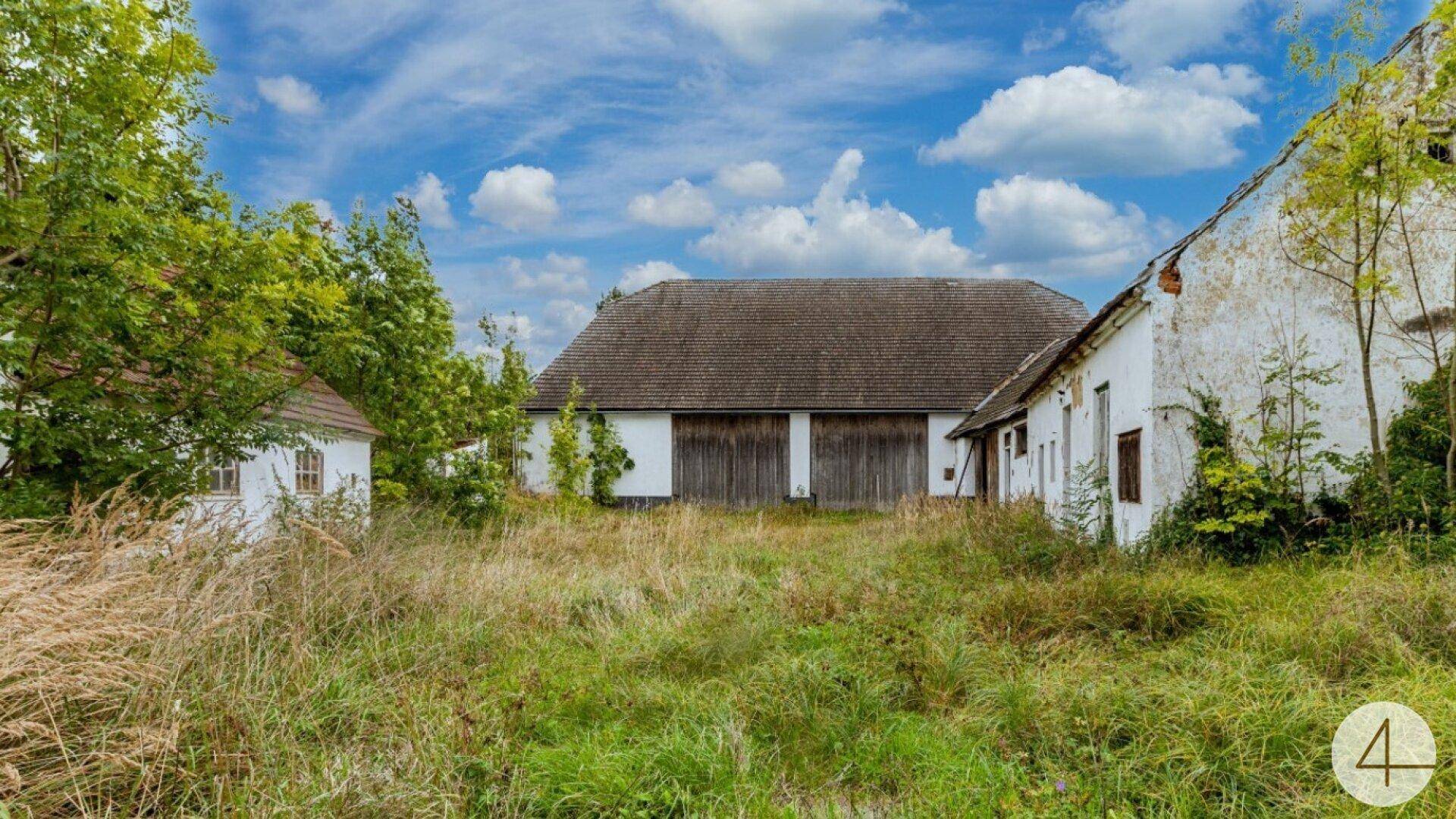 Alte, ländliche Gebäude mit verputzten Fassaden und einem großen, verwilderten Grundstück.