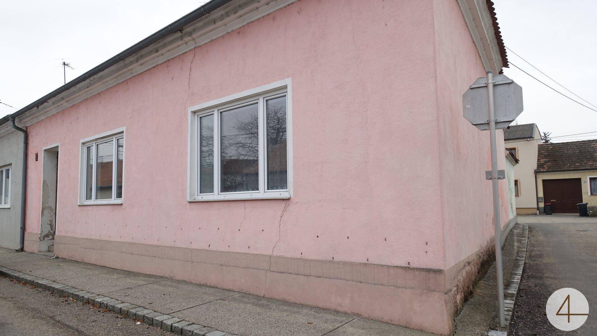 Fassade eines rosafarbenen Hauses mit weißen Fenstern und einem Bürgersteig an einer ruhigen Straße.