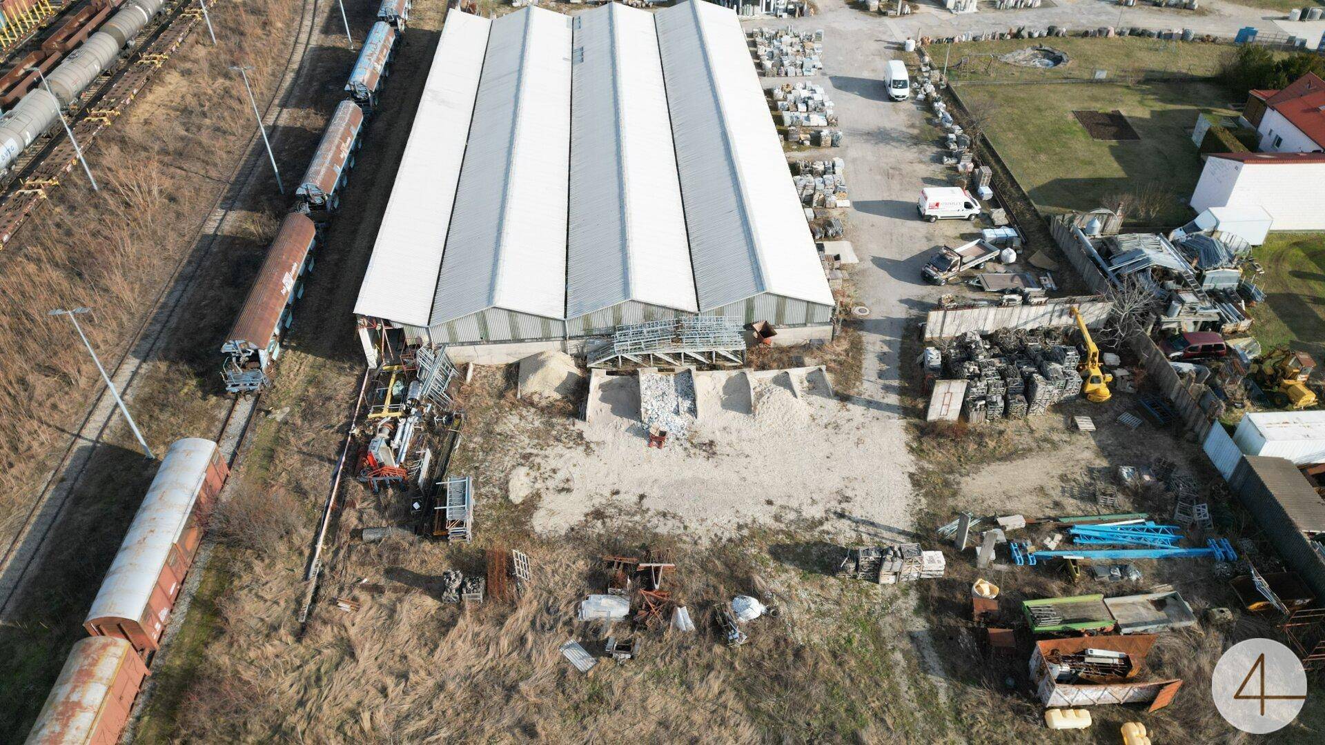 Luftaufnahme einer großen Lagerhalle direkt an Bahngleisen mit abgestellten Güterwaggons.