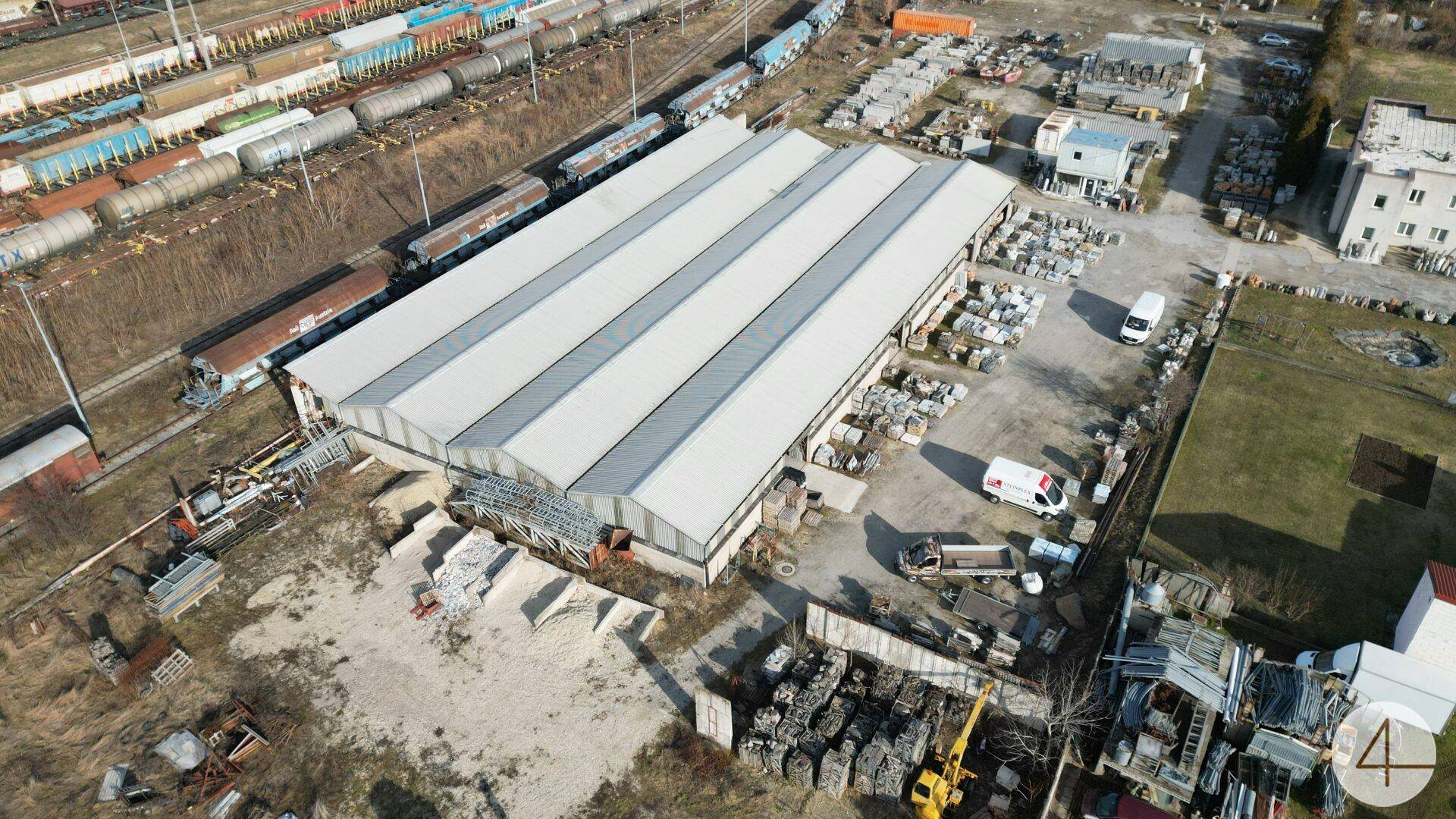 Weitläufige Luftaufnahme eines Gewerbegebiets mit großer Lagerhalle und Güterzügen im Hintergrund.