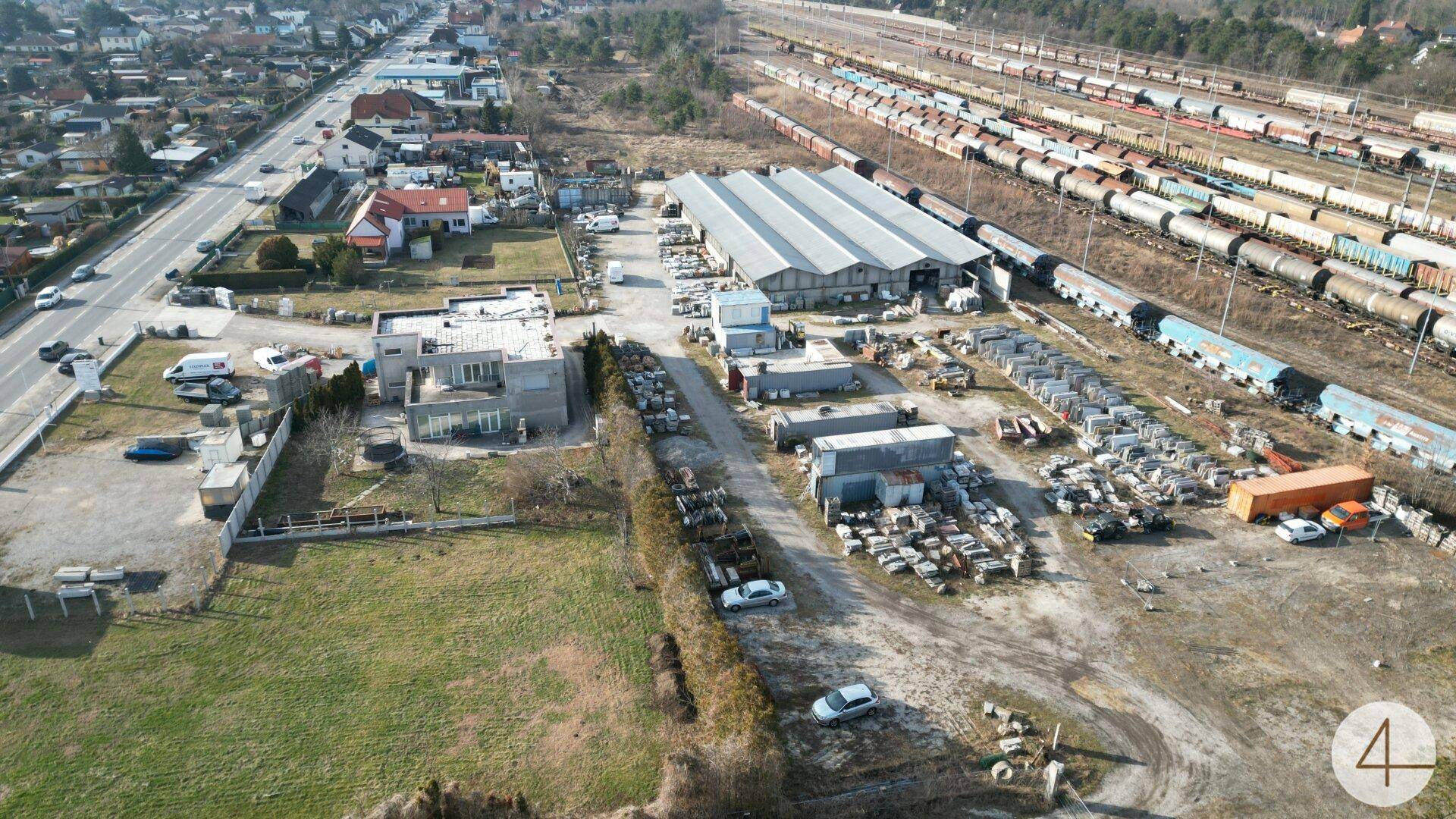 Gesamtansicht eines Gewerbegebiets mit Gebäuden, Lagerflächen, Bahngleisen und einer Hauptstraße.