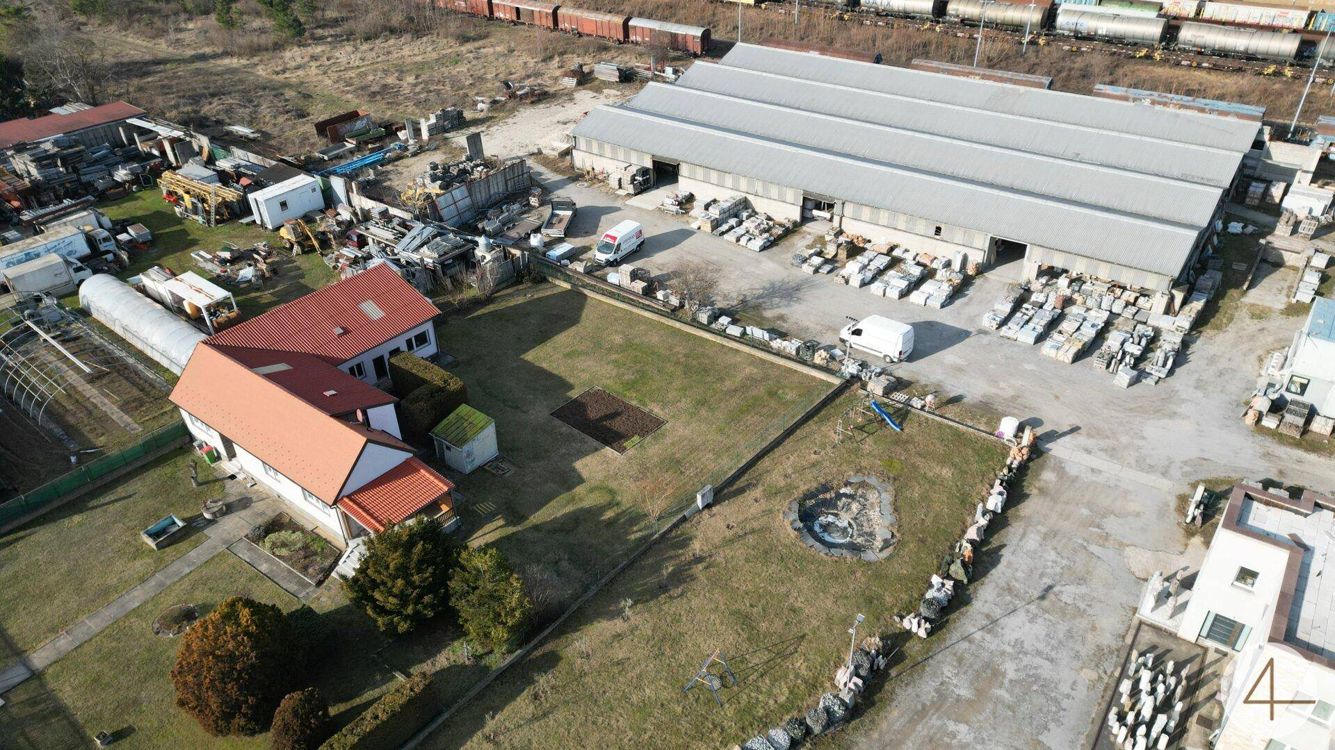 Luftaufnahme eines Wohnhauses mit Garten neben einem Industriegebäude und Bahngleisen.