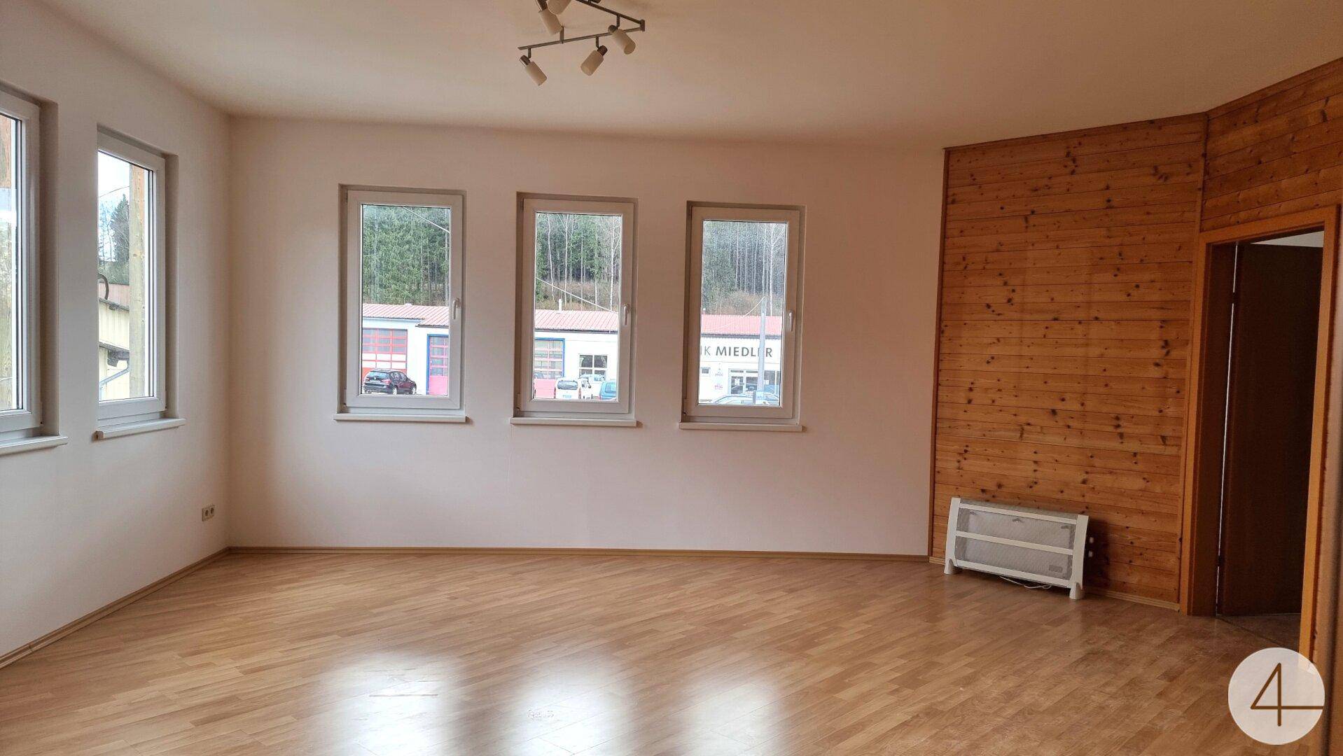 Geräumiges Wohnzimmer mit Holzboden, Holzvertäfelung und mehreren Fenstern, die viel natürliches Licht hereinlassen.