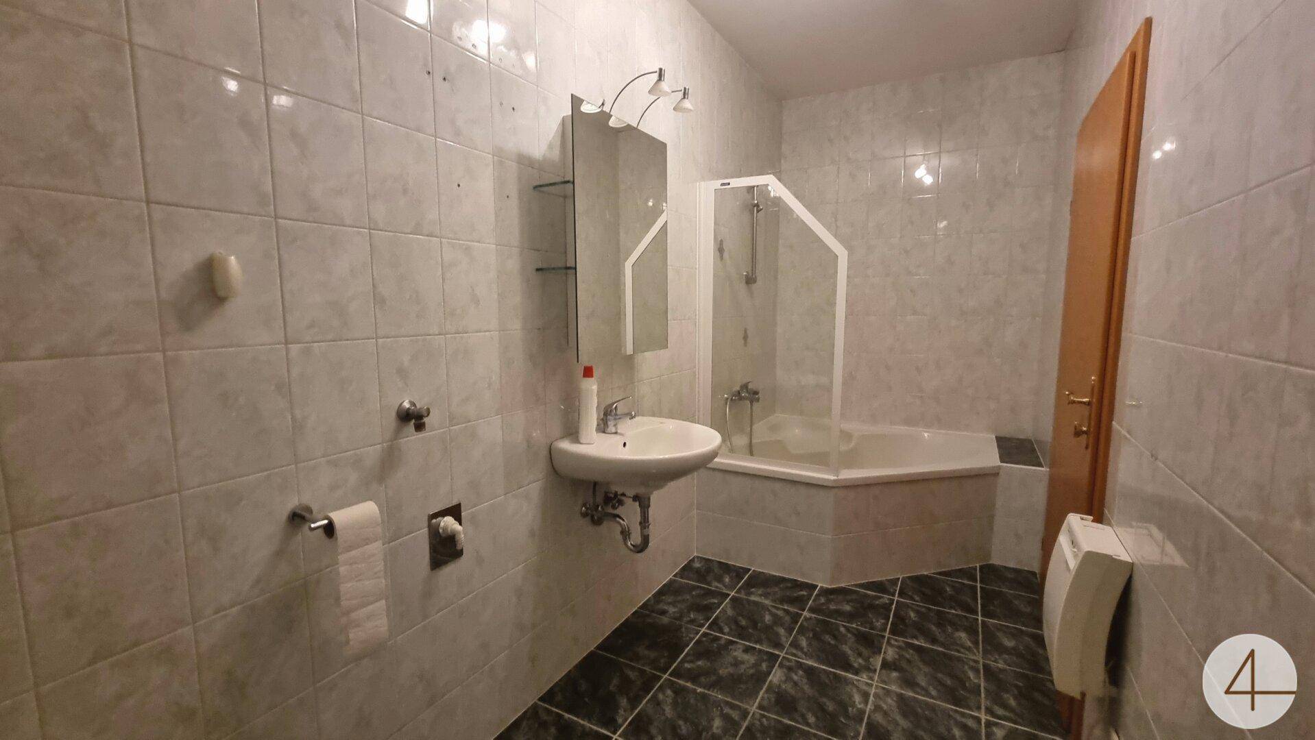 Badezimmer mit Eckbadewanne, Duschkabine und gefliesten Wänden und Böden in hellen und dunklen Grautönen.