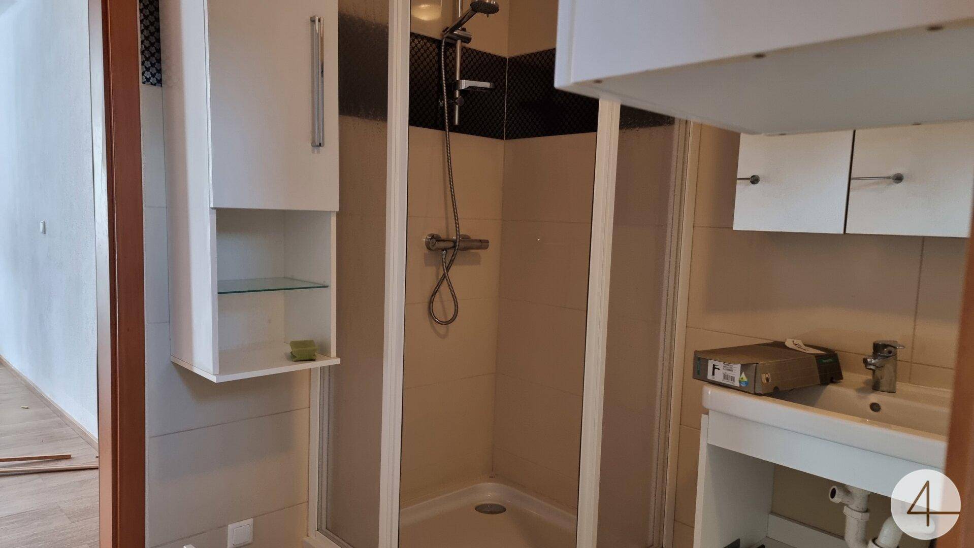 Kleines Badezimmer mit Duschkabine, Waschbecken und Spiegelschrank, funktional und hell gefliest.