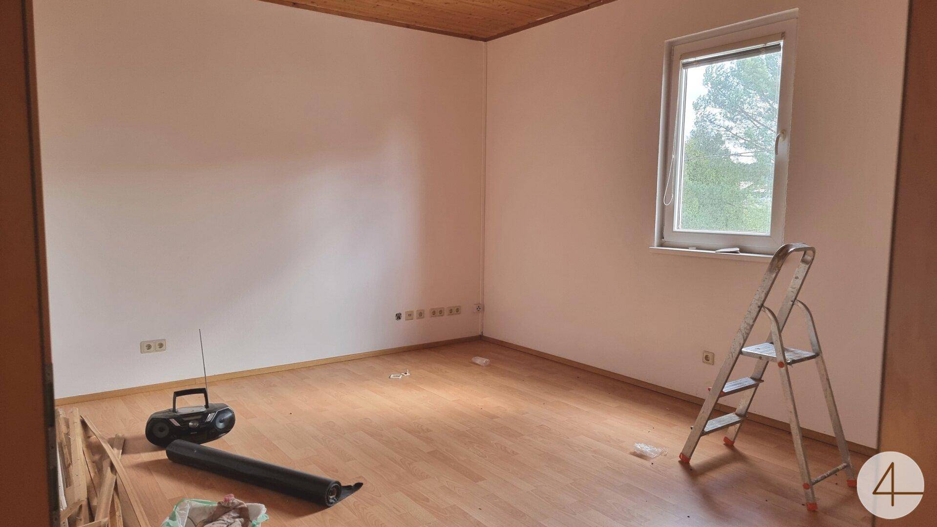 Heller Raum mit Laminatboden und Holzdecke, ein Fenster bietet einen angenehmen Blick ins Grüne.