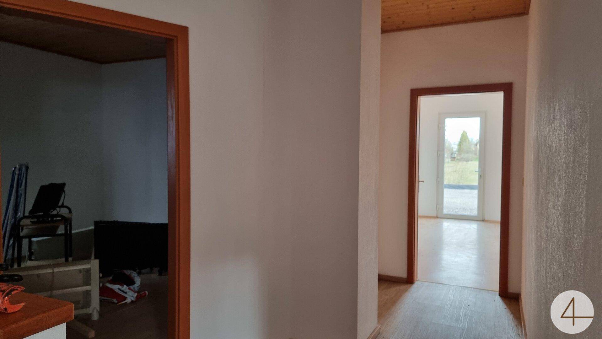 Flur mit Holztüren und Laminatboden, der zu verschiedenen Räumen und einem Ausgang ins Freie führt.