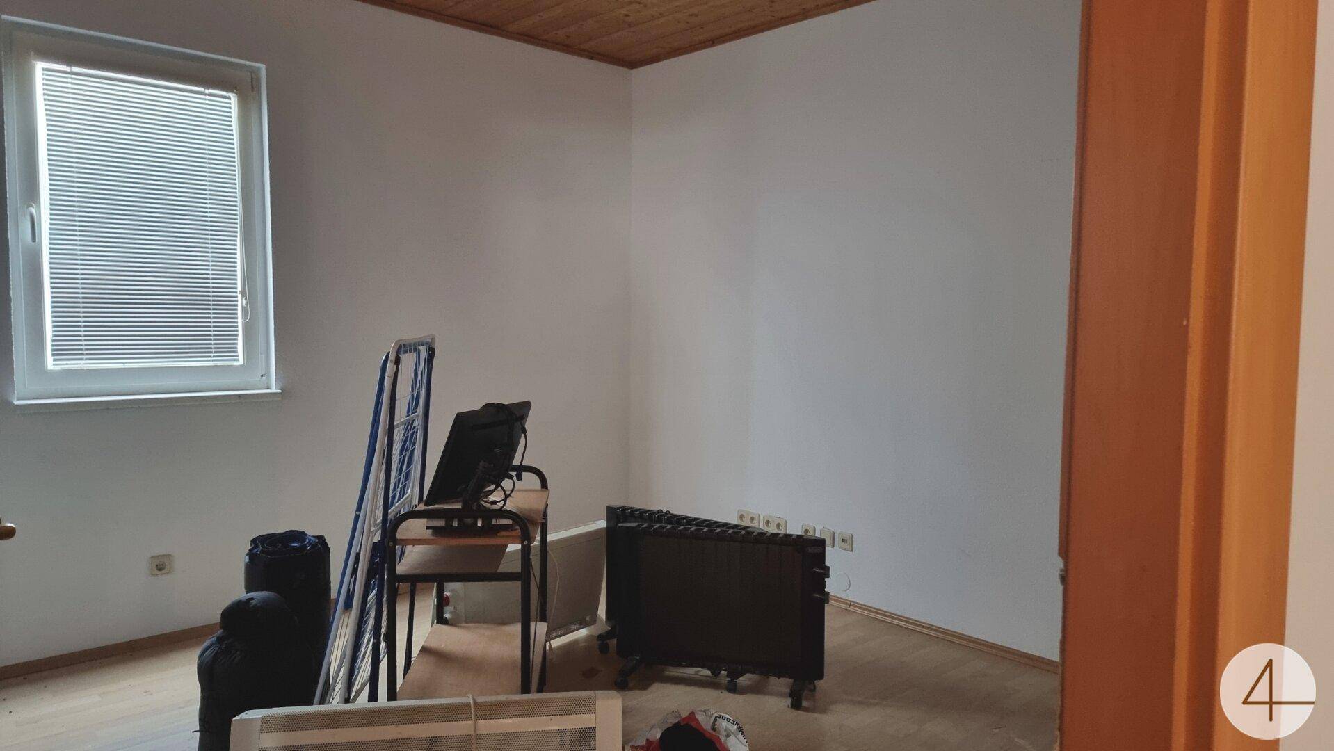 Leerer Raum mit Laminatboden und einem Fenster mit Jalousien, bereit zur individuellen Einrichtung.