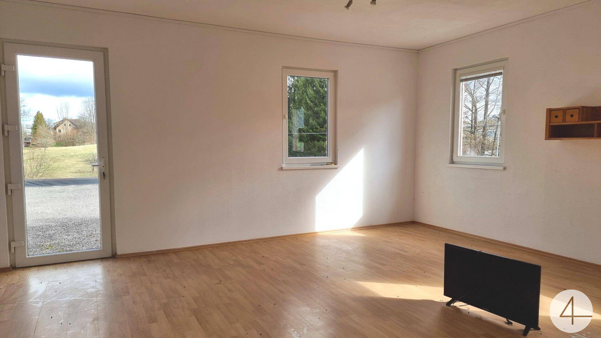 Heller Raum mit Laminatboden und einer Glastür, die direkten Zugang zum Außenbereich und Garten bietet.