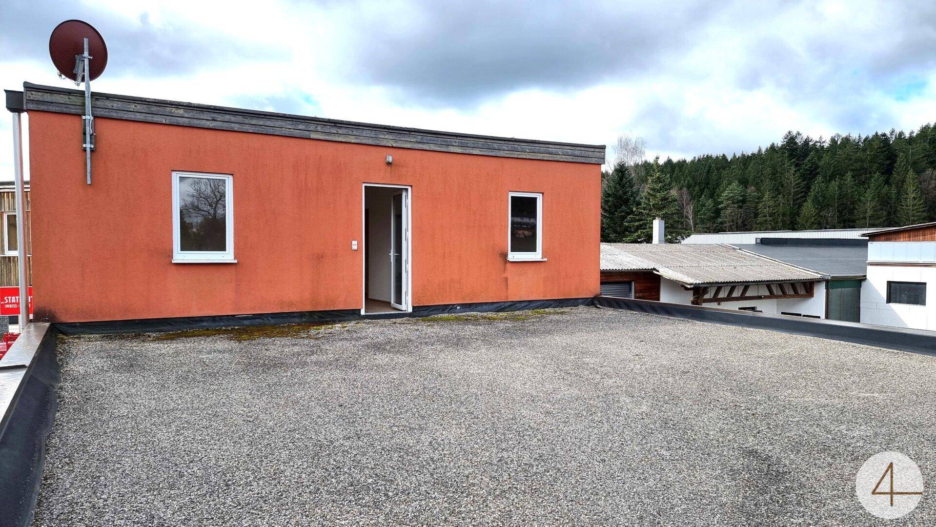 Große Dachterrasse mit Kiesbelag und einem Gebäude mit roter Fassade und Fenstern, ideal für Entspannung.