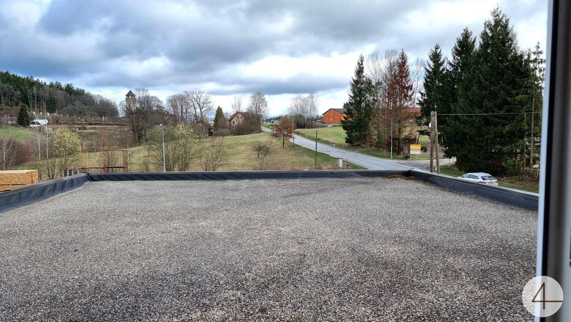 Weitläufiger Blick von der Dachterrasse auf die umliegende Landschaft mit Bäumen, Feldern und Häusern.