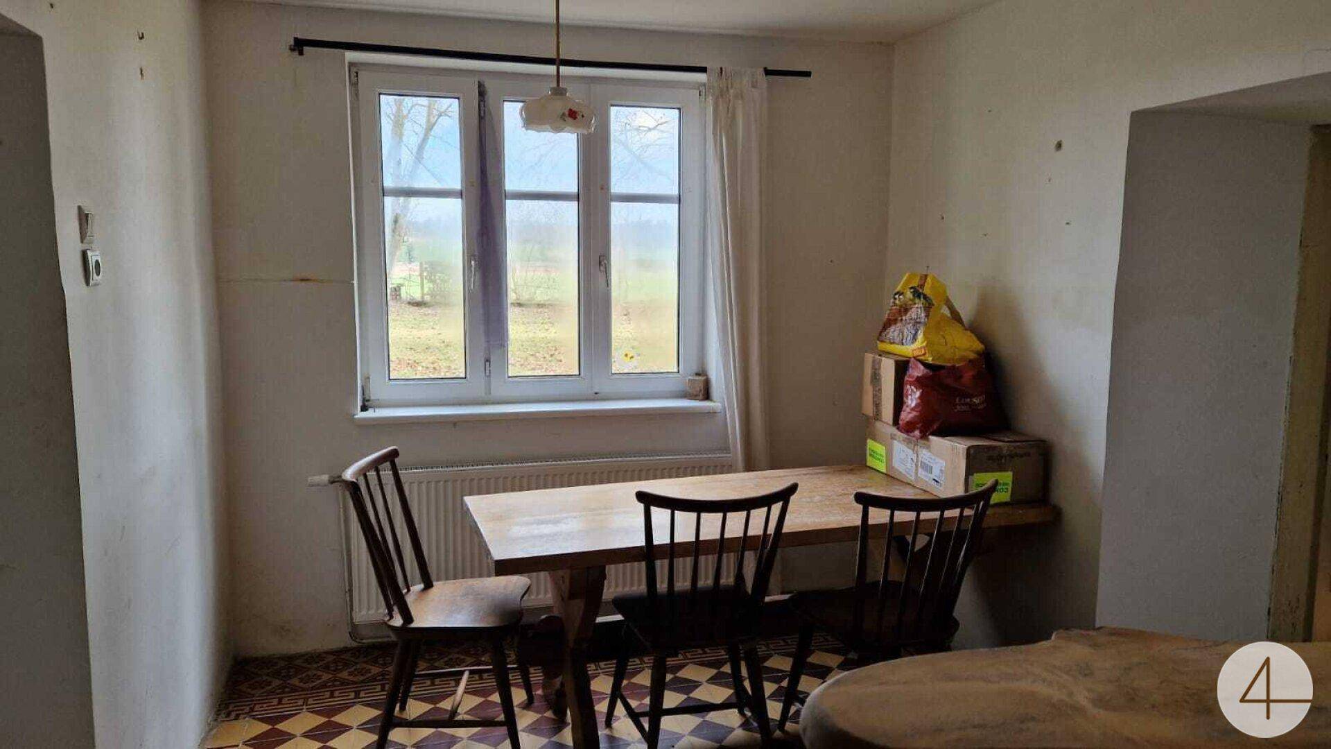 Einfacher Essbereich mit Holztisch und Stühlen, beleuchtet durch ein Fenster.