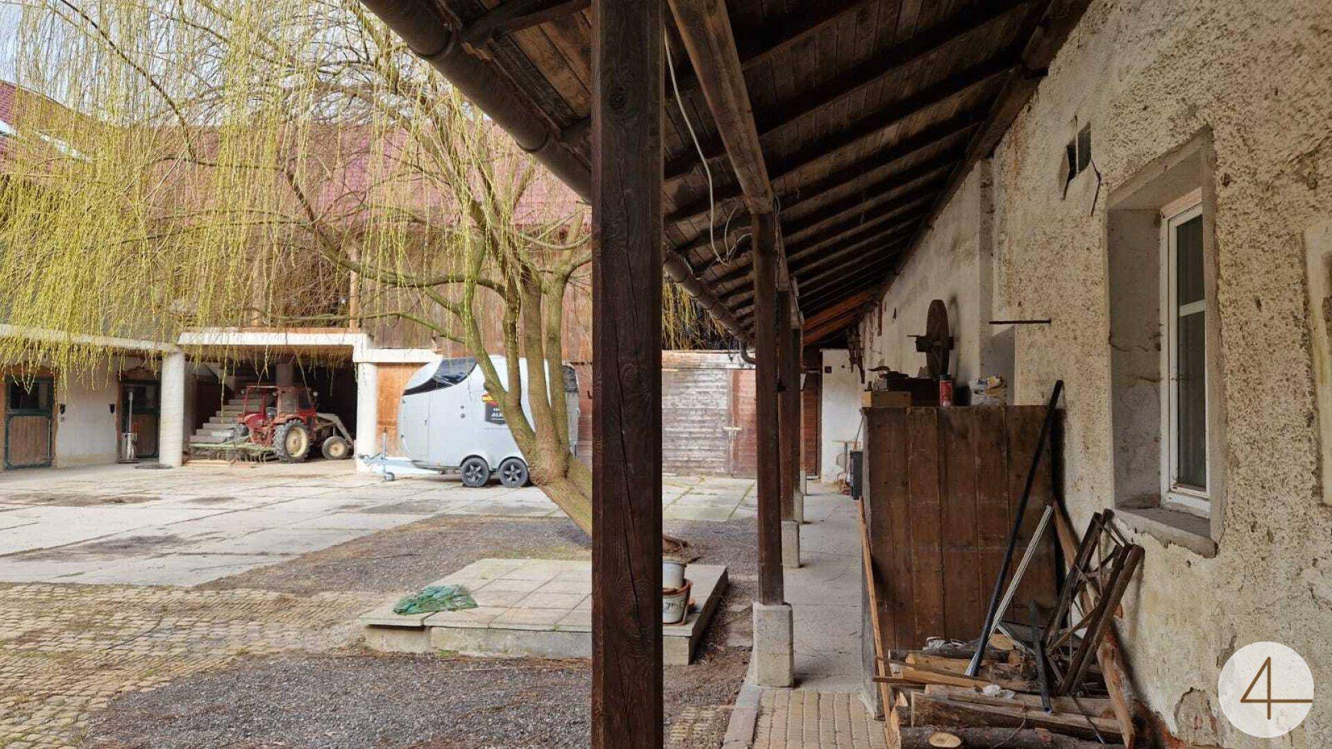 Alter Innenhof eines Bauernhofs mit überdachtem Gang und landwirtschaftlichen Fahrzeugen.