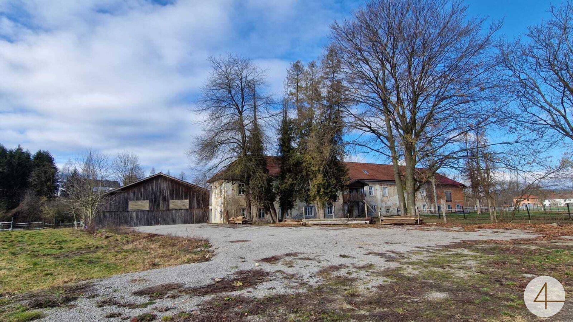 Historisches Anwesen mit großem Gebäude, Schotterplatz und alten Bäumen in ländlicher Umgebung.