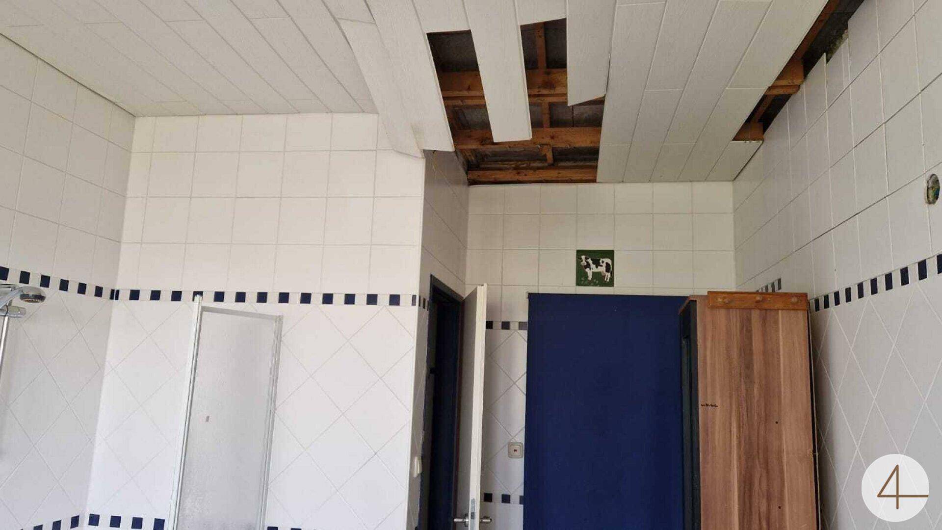 Badezimmer mit weißen Fliesen und einer beschädigten Decke, die Reparaturen benötigt.