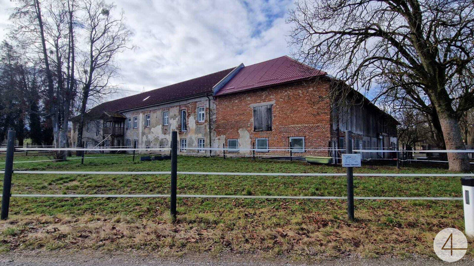 Großes historisches Gebäude mit Ziegel- und Putzfassade, umgeben von einem Zaun.