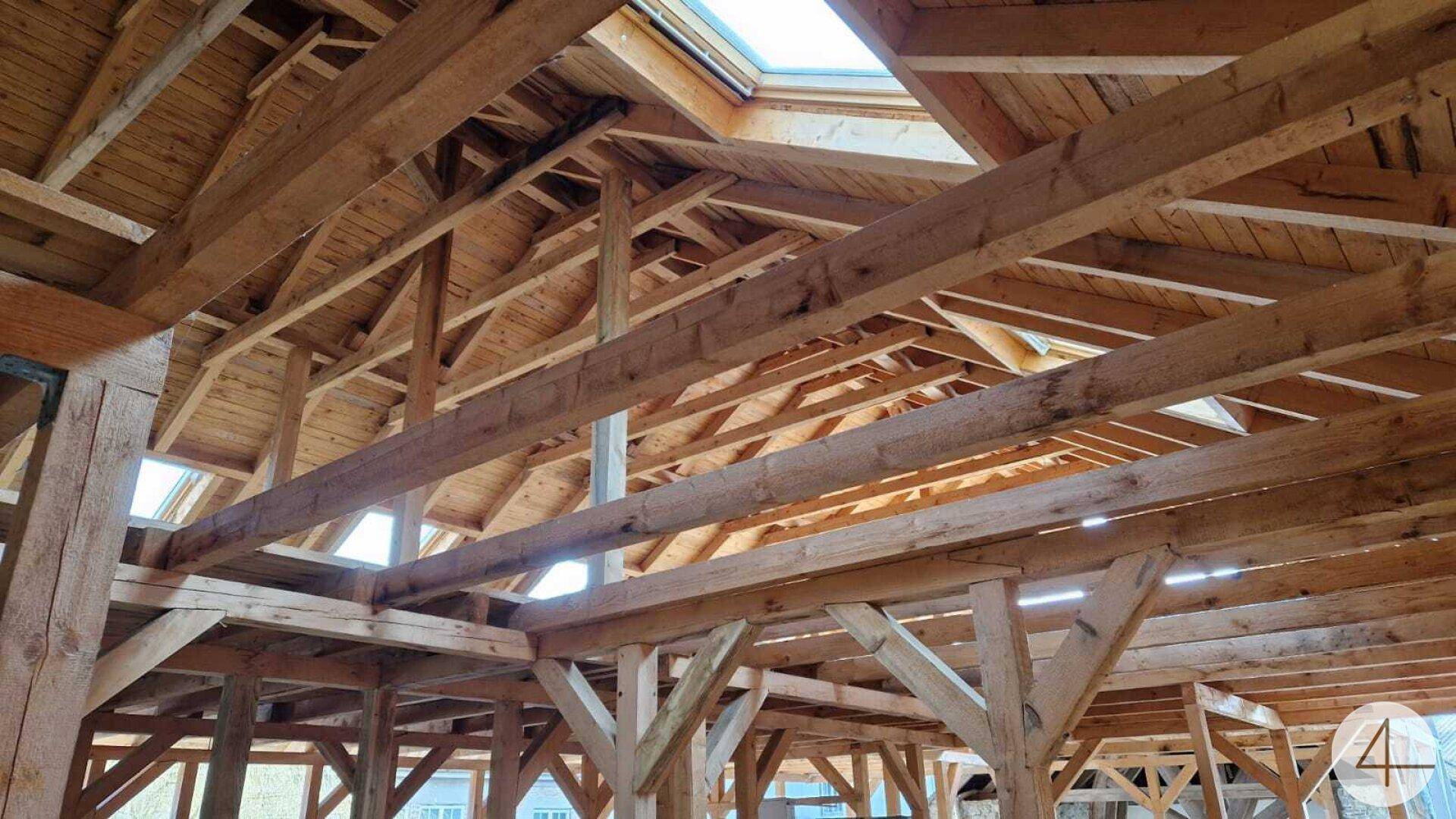 Offene Holzkonstruktion eines Dachstuhls mit sichtbaren Balken und Dachfenstern.