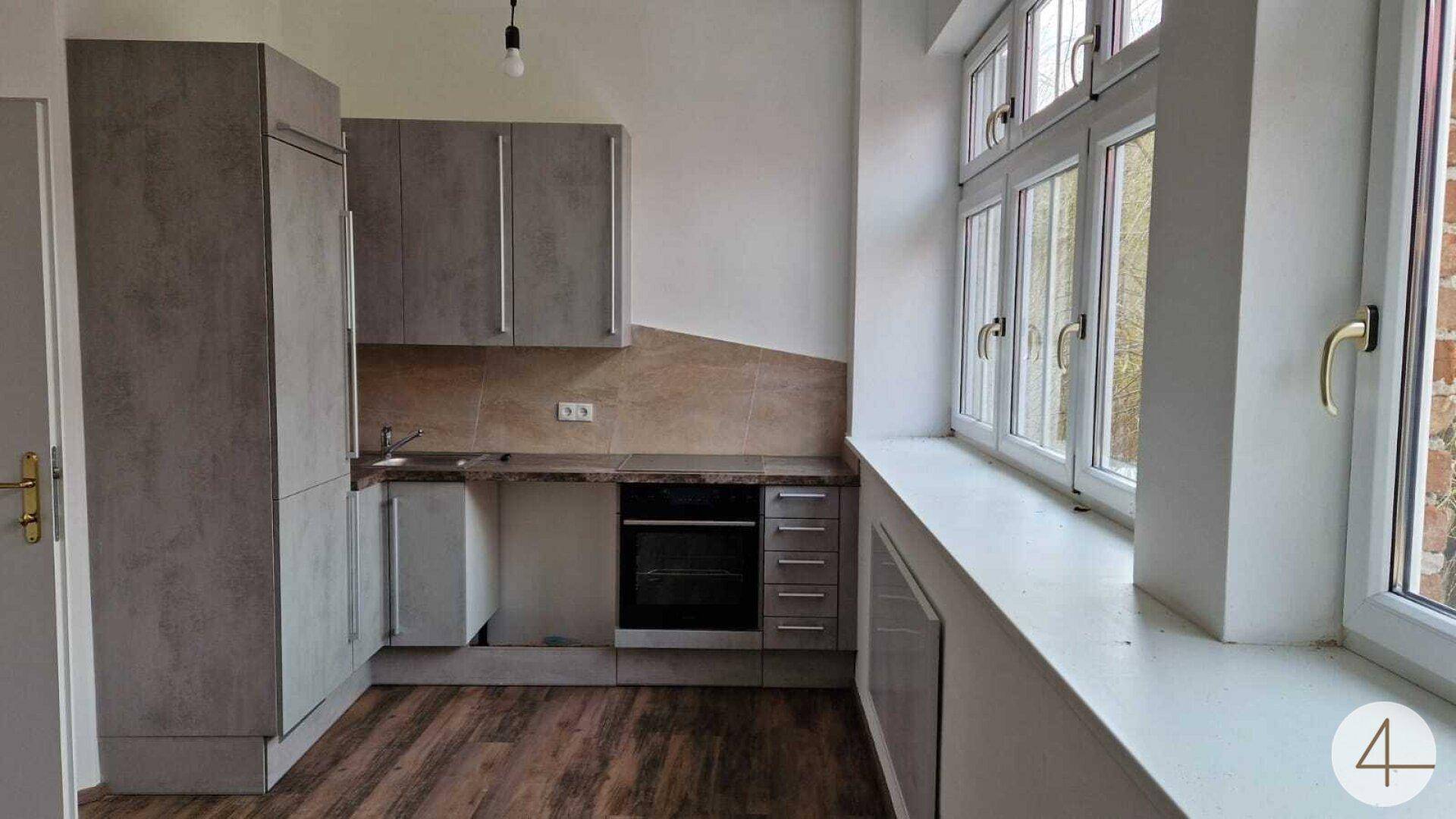 Küche mit grauen Schränken, Einbauofen und Fenster, ausgestattet mit Laminatboden in Holzoptik.