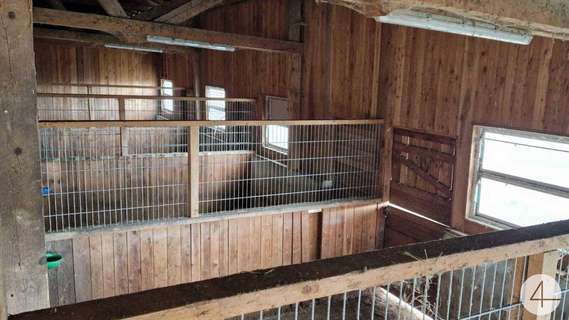 Blick von oben in eine Scheune oder einen Stall mit Holzkäfigen und Metallgittern, die die Bereiche abgrenzen.