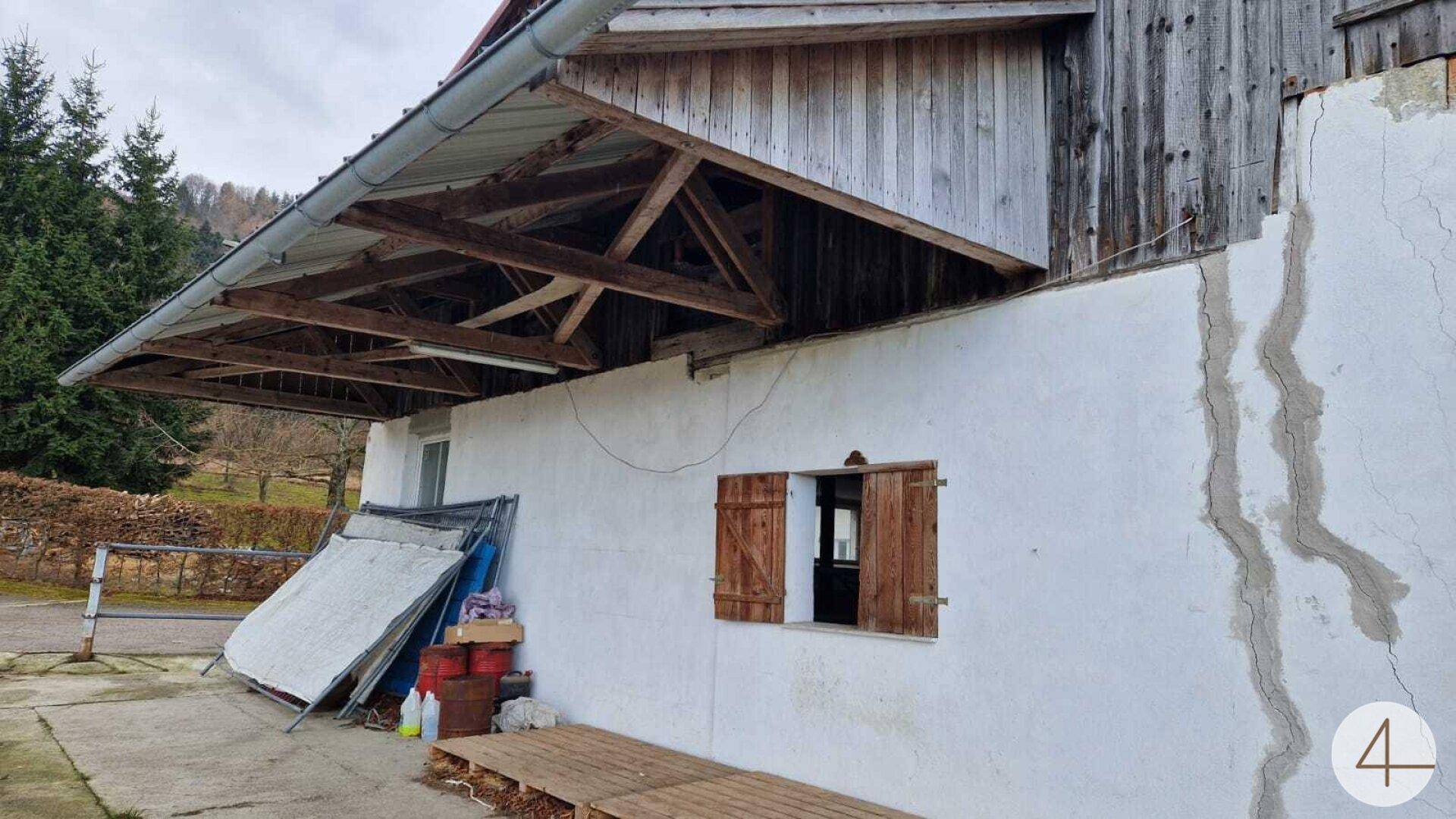 Teilansicht eines Gebäudes mit Holzbalkenkonstruktion, weißer Wand und einem Fenster mit Holzläden.