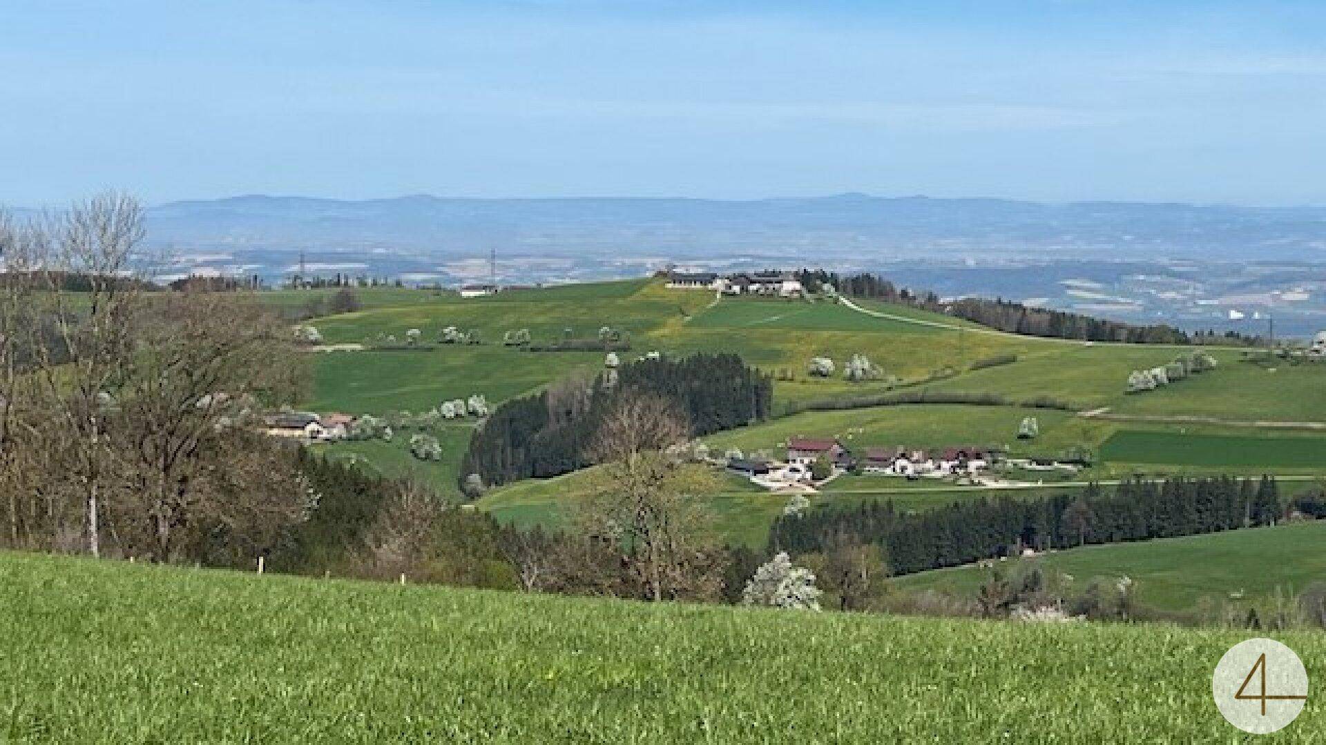 Weitläufige grüne Hügellandschaft mit verstreuten Häusern und Dörfern bis zum fernen Horizont.
