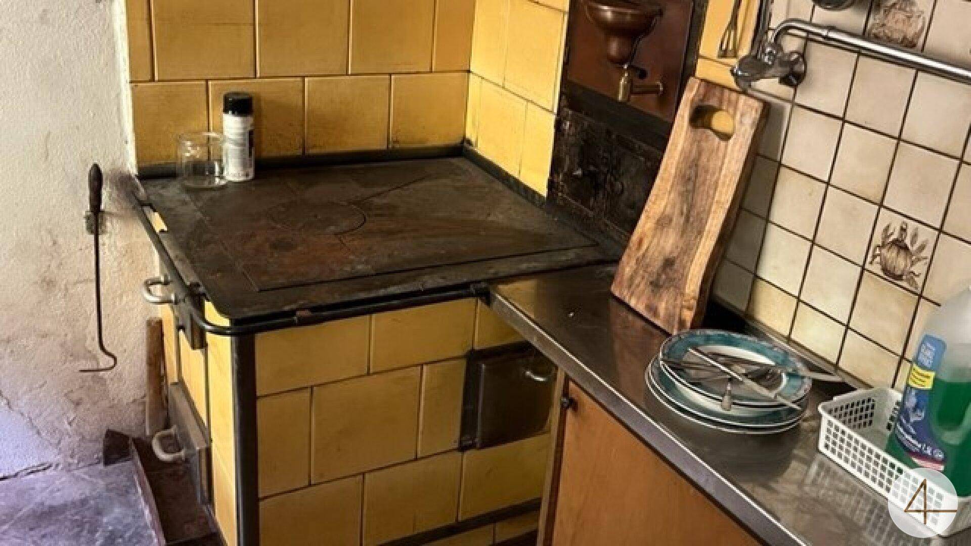 Rustikale Küche mit einem traditionellen gelben Kachelofen als Kochstelle und einfacher Spüle.