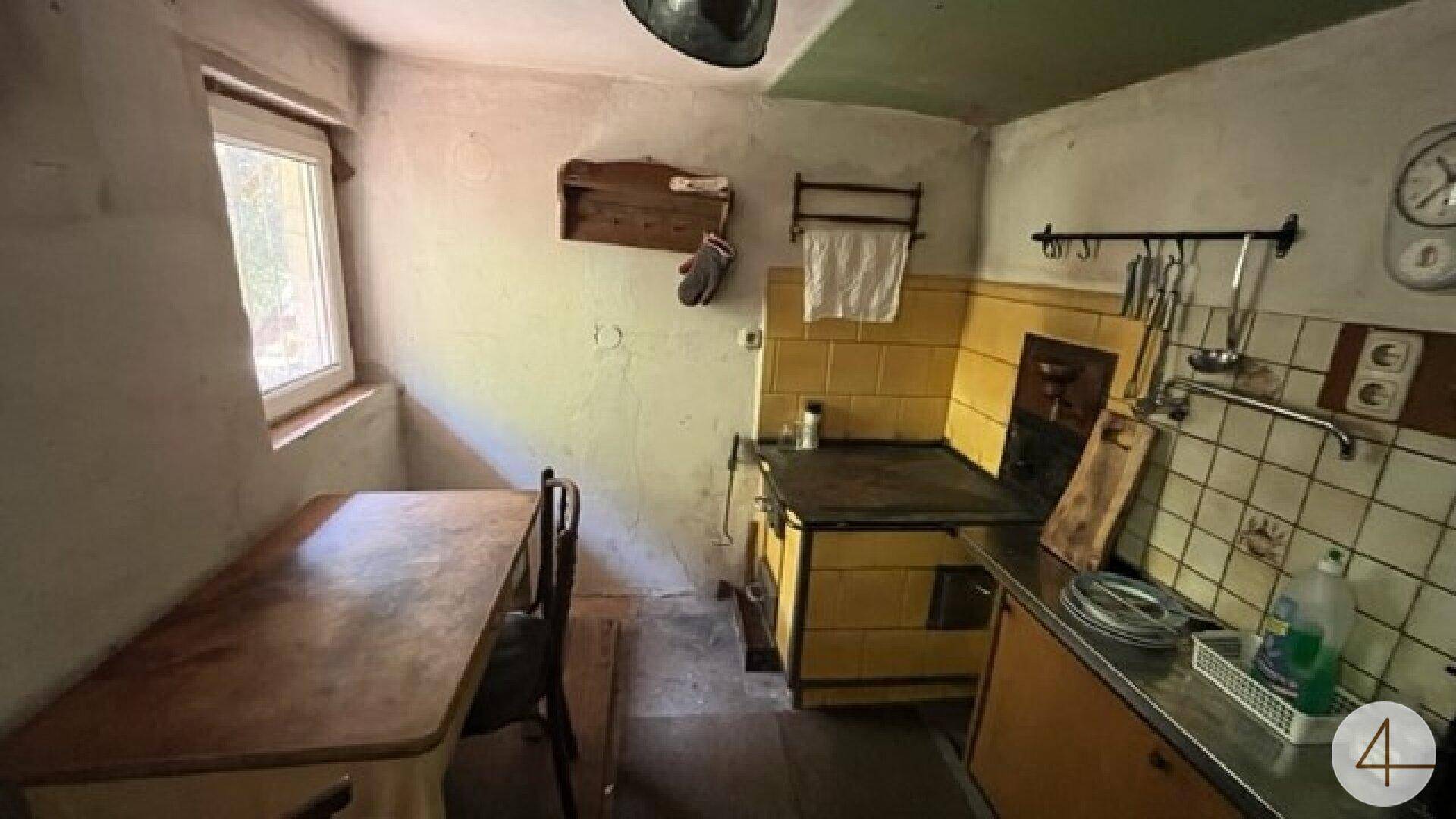 Gemütliche, traditionelle Küche mit gelben Fliesen, einem alten Holzofen und einem kleinen Esstisch am Fenster.