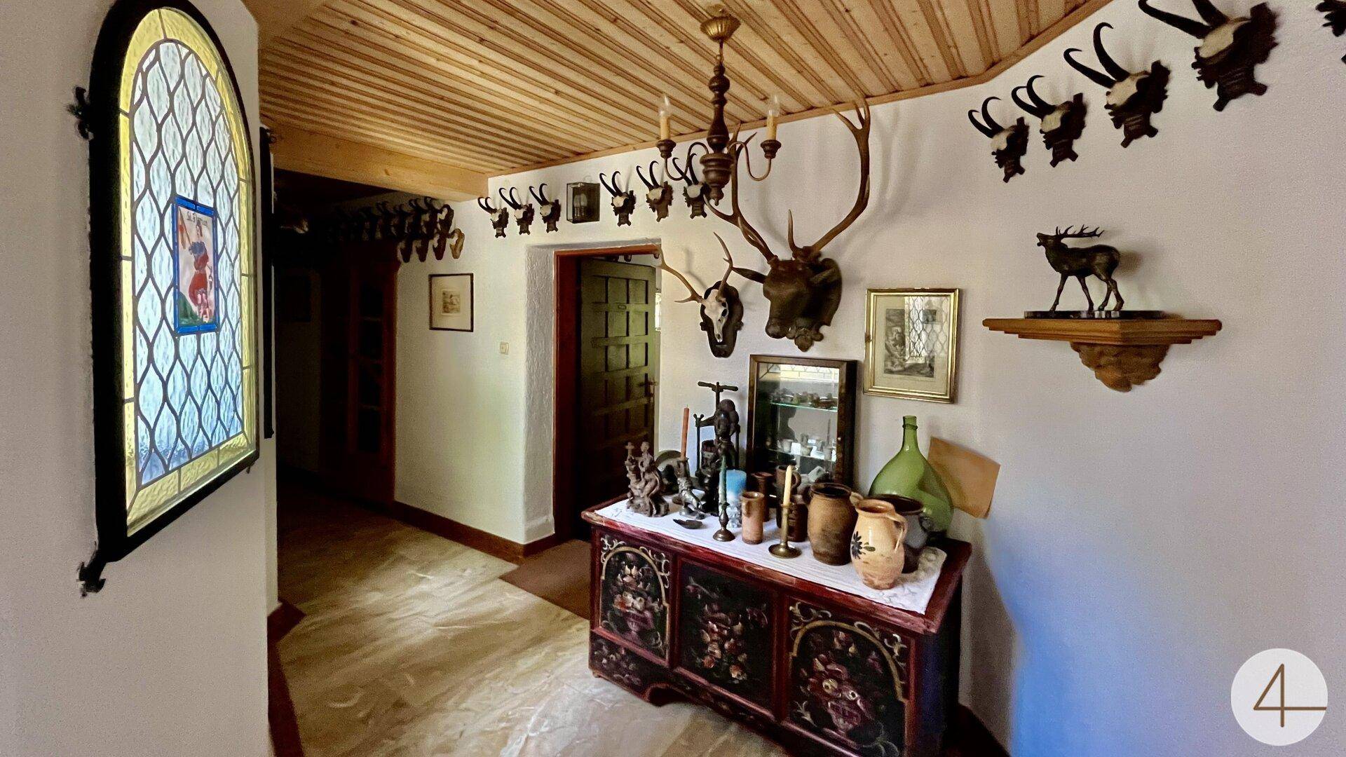 Rustikaler Flur mit Holzbalkendecke, Jagdtrophäen und einem farbigen Bleiglasfenster.