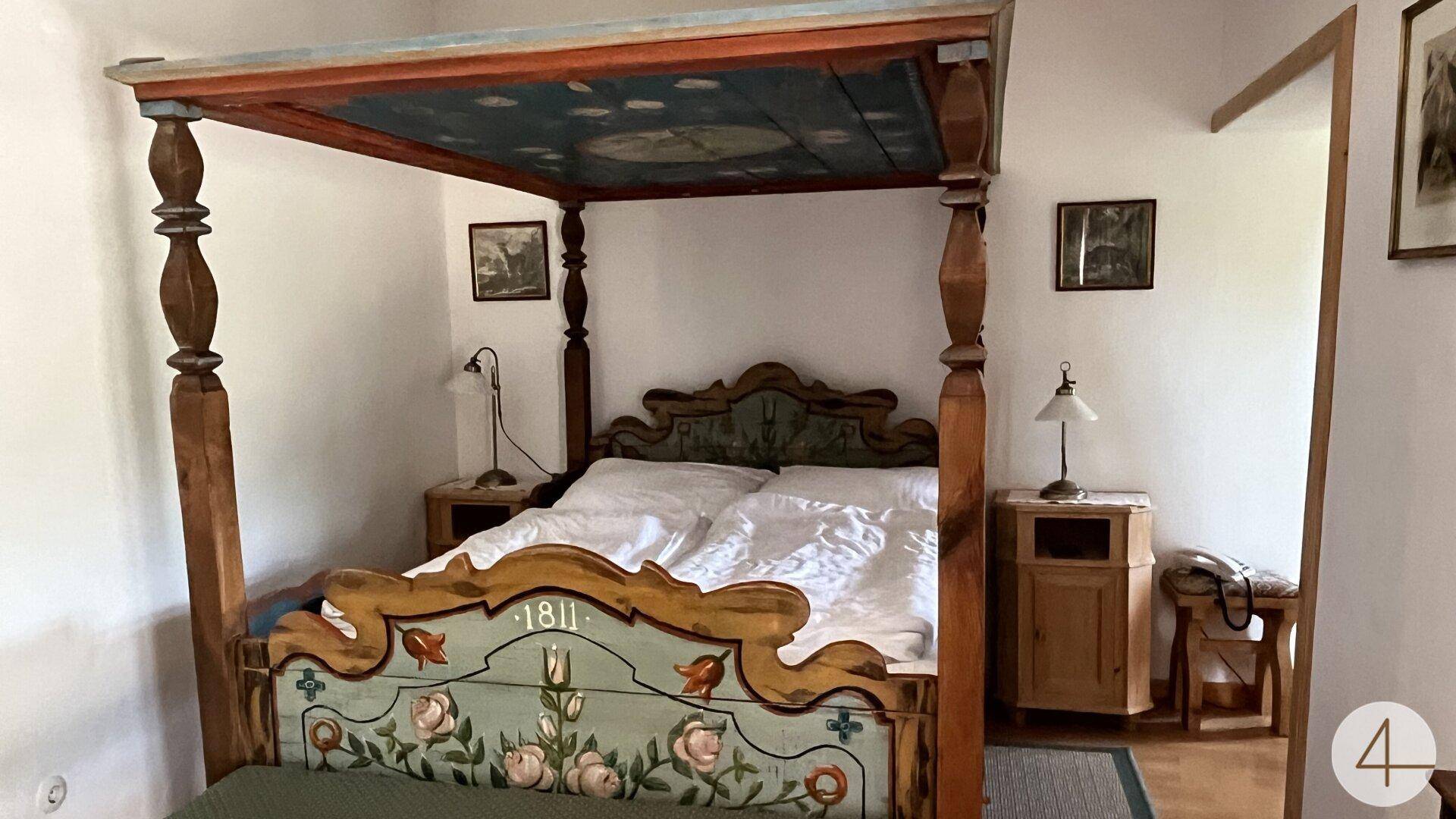 Schlafzimmer mit einem kunstvoll bemalten Himmelbett und traditionellen Holzmöbeln.