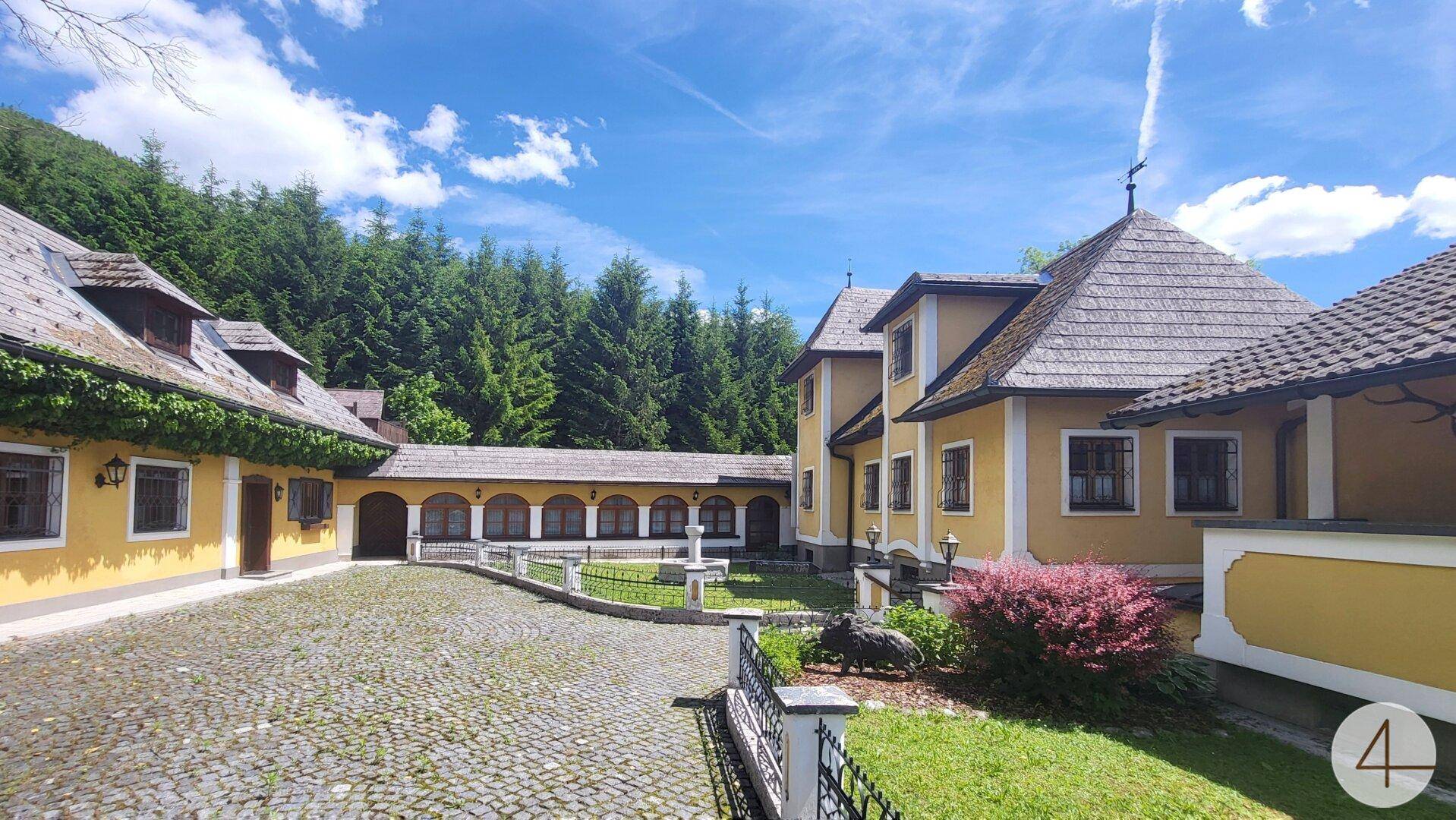 Historisches Anwesen mit gelber Fassade, gepflastertem Innenhof und umgebender Natur.