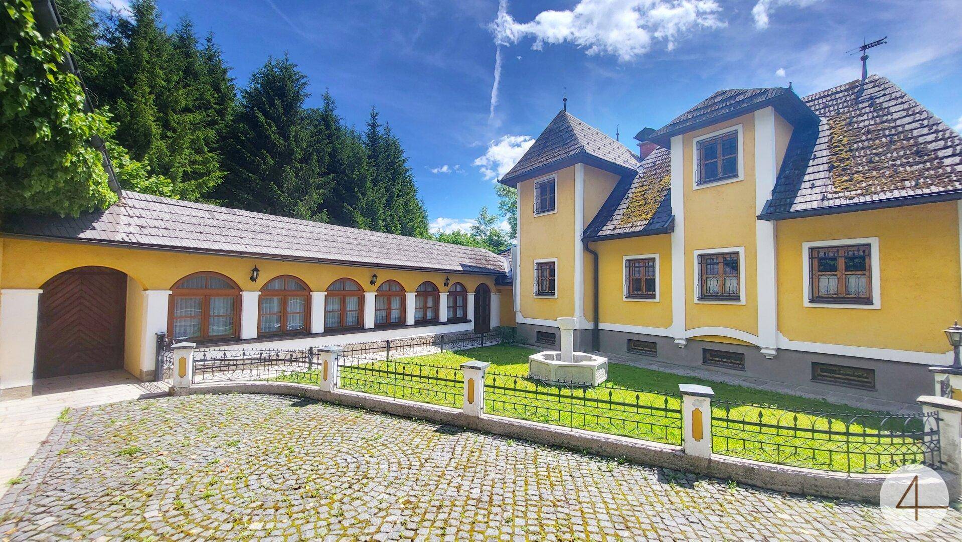 Historisches Anwesen mit gelber Fassade, gepflastertem Innenhof und einem dekorativen Brunnen.
