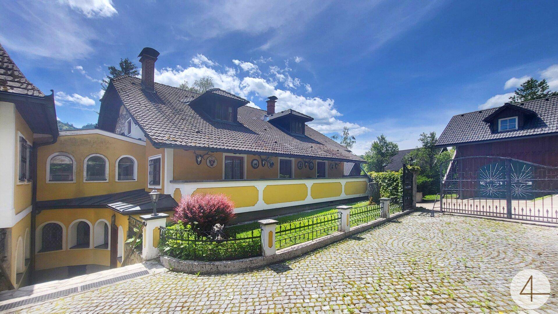Historisches Anwesen mit gelber Fassade, gepflastertem Innenhof und einem schmiedeeisernen Tor.